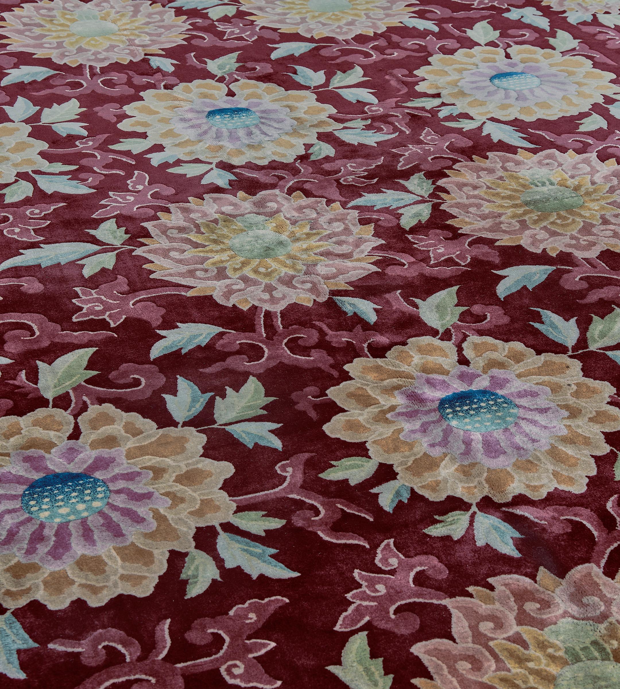 This traditional hand-woven Chinese rug has a merlot-colored overall field with diagonal rows of refined saffron and dusty pink floral pendants issuing long fronds forming a lattice pattern, in a complementary wine colored border of similar floral