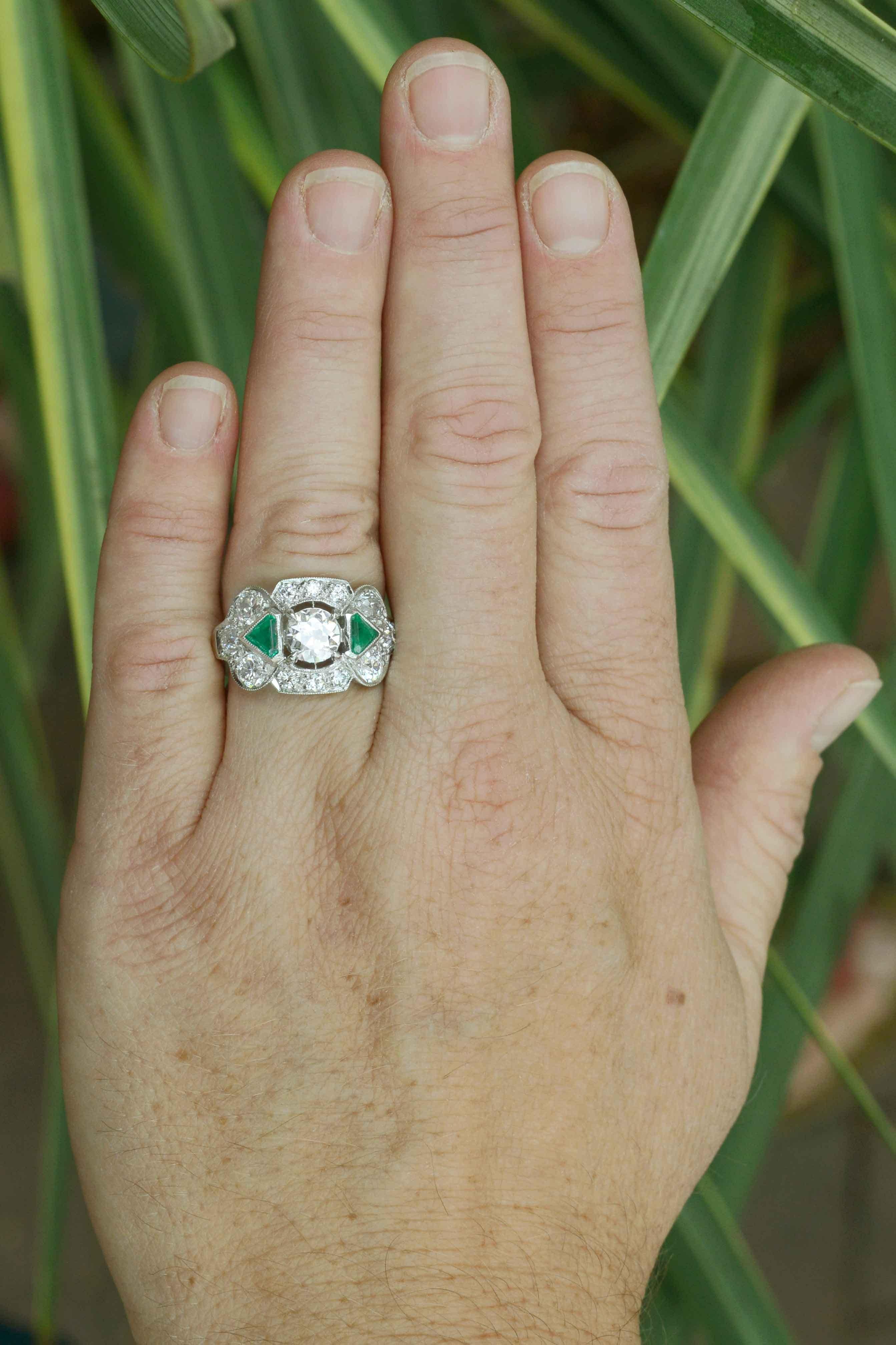 A unique Art Deco diamond and emerald three stone engagement ring. Centered by a captivatingly brilliant 1 carat old European diamond flanked by a pair of lush, vivid green emerald triangles. As if that wasn't enough, this 1920s Jazz Age heirloom is