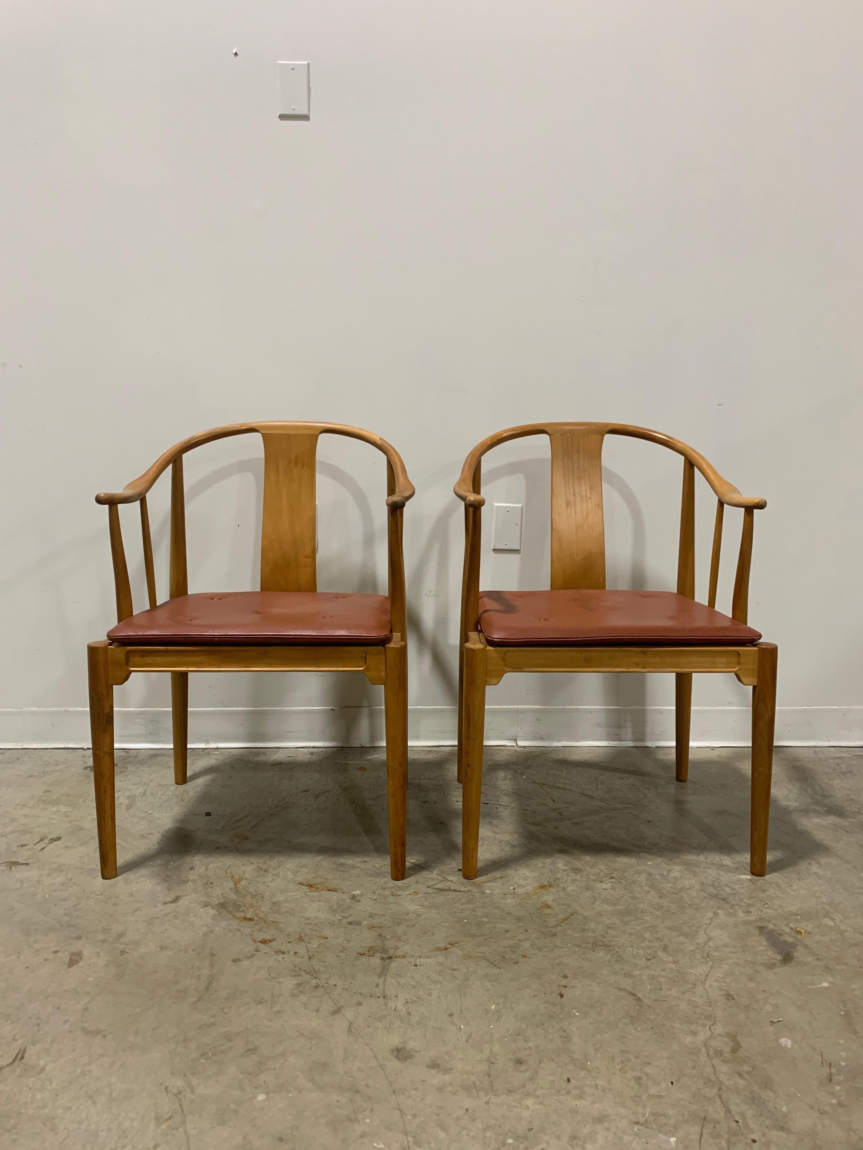 Highly collectable 1944 design by Hans Wegner- an interpretation of traditional Chinese style chairs. Slender natural cherry frames with a leather seat pad supported by webbing. Minimalist design sold by Illums Bolighus in Copenhagen, Denmark. Both