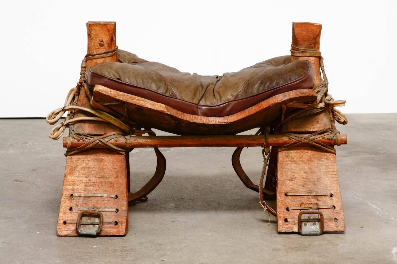 19th century authentic camel saddle stool seat from Morocco. Features a rustic wooden frame reinforced with leather rawhide strapping. This is not a tourist reproduction but a real camel saddle that has been used for decades. Topped with a deep