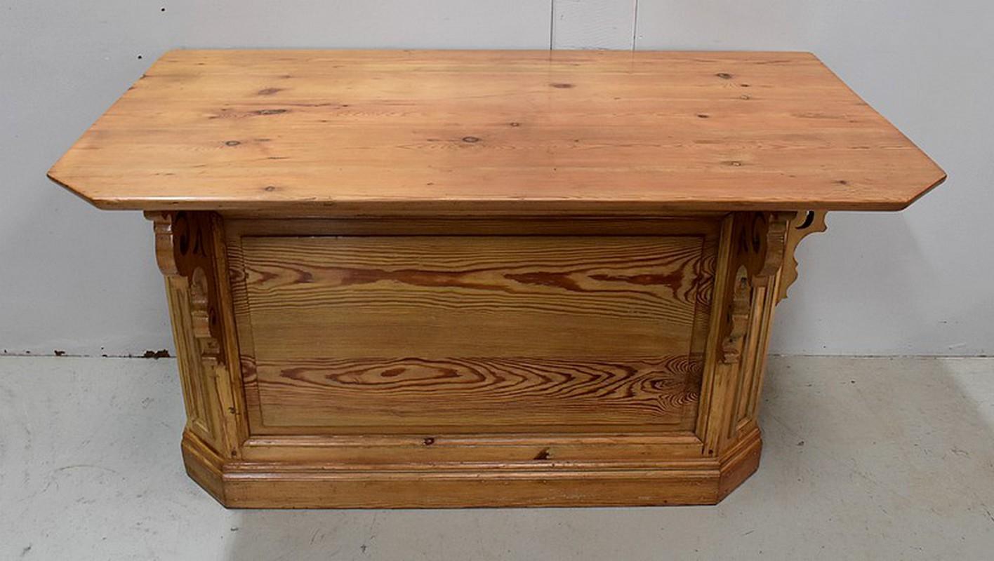 Natural pine shop counter with a top with cut front corners. This top is wider on the left than it is on the right. It is supported at the front and on one side by openwork scrolled consoles.

The fronts of this piece of furniture are composed of