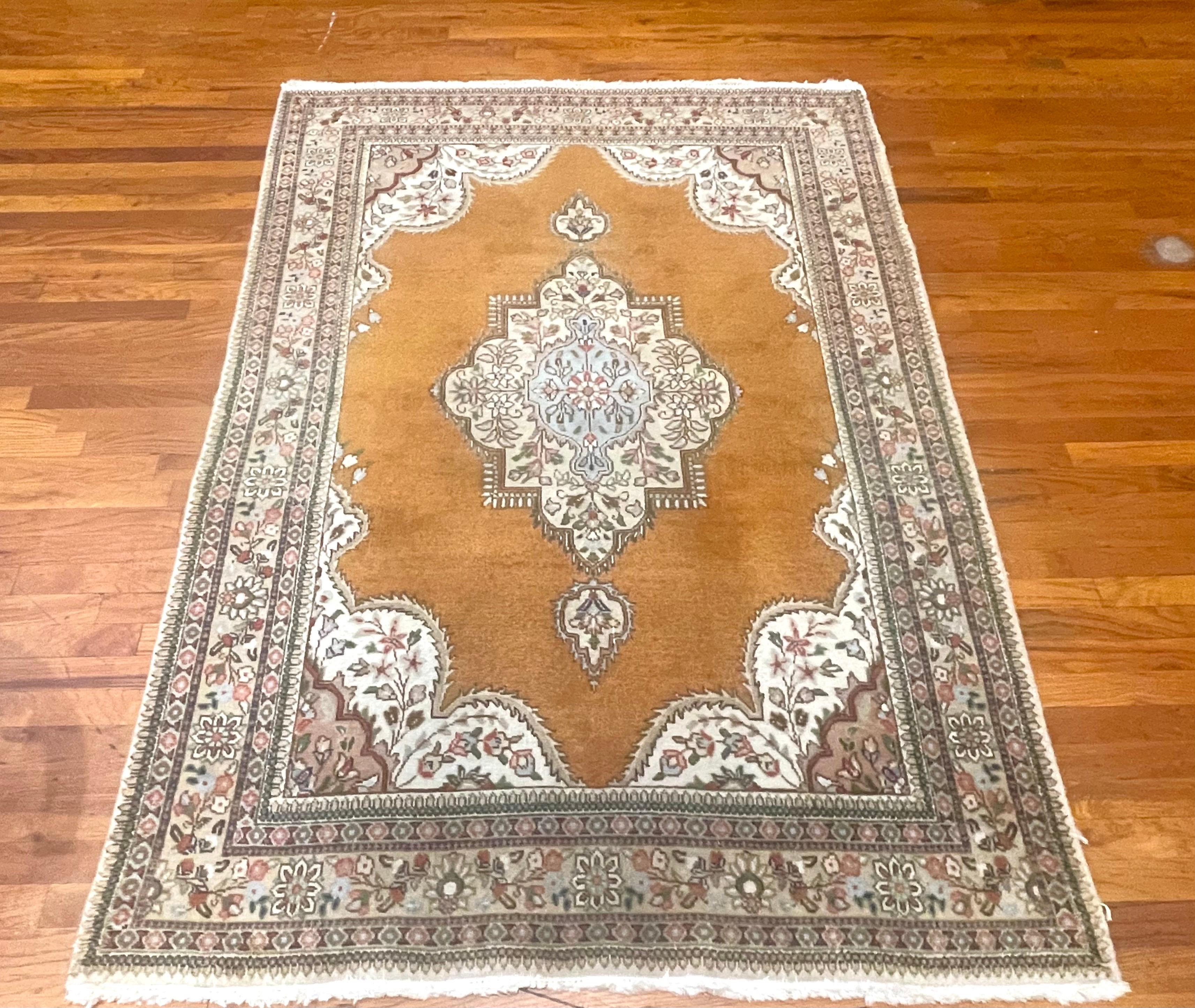 Wir stellen einen handgeknüpften persischen Täbriz-Teppich vor, der für sein Design und seine Qualität bekannt ist. Dieser Teppich mit offenem, ausgefeiltem Blumenmedaillon hat einen Wollflor mit Baumwollgrund. Die Grundfarbe ist senfgelb und die
