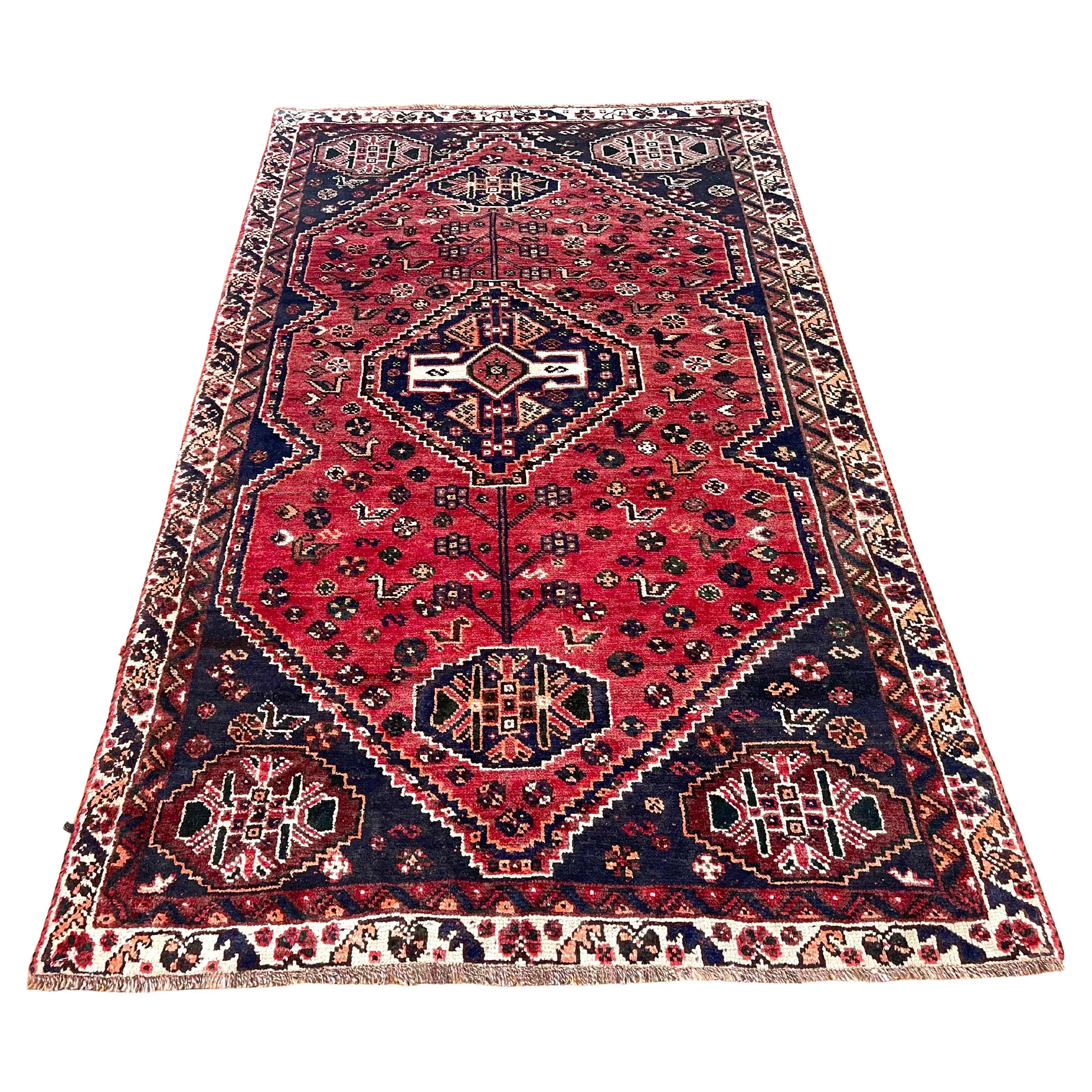 Dieser schöne Teppich ist ein authentisches Stück aus Shiraz, Iran, einer Region, die für ihre reiche Tradition handgewebter Teppiche bekannt ist. Ganz aus Wolle gefertigt, zeigen sowohl der Flor als auch der Unterbau die Strapazierfähigkeit und den
