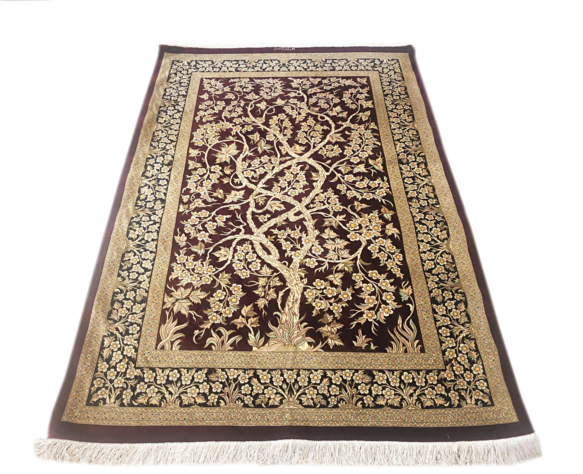 Ce tapis extrêmement fin a été tissé dans la ville de Qum, en Iran. Ce tapis, dont les poils et le fond sont en soie, présente un spectaculaire motif d'arbre de vie tissé sur un fond bordeaux avec une bordure bleu foncé. L'arbre de vie est un