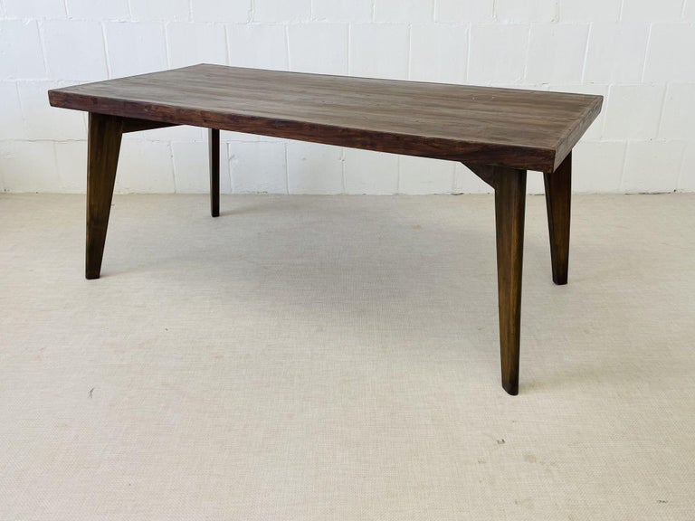 Pierre Jeanneret Dining Table, Model PJ-TA-01-A
 
Minimalist dining table (6' x 3') featuring a solid thick teak top with a curved lower corner and two pairs of slanted, tapered legs, connected by two V-shaped crosspieces under the tops. 
 
 Part of