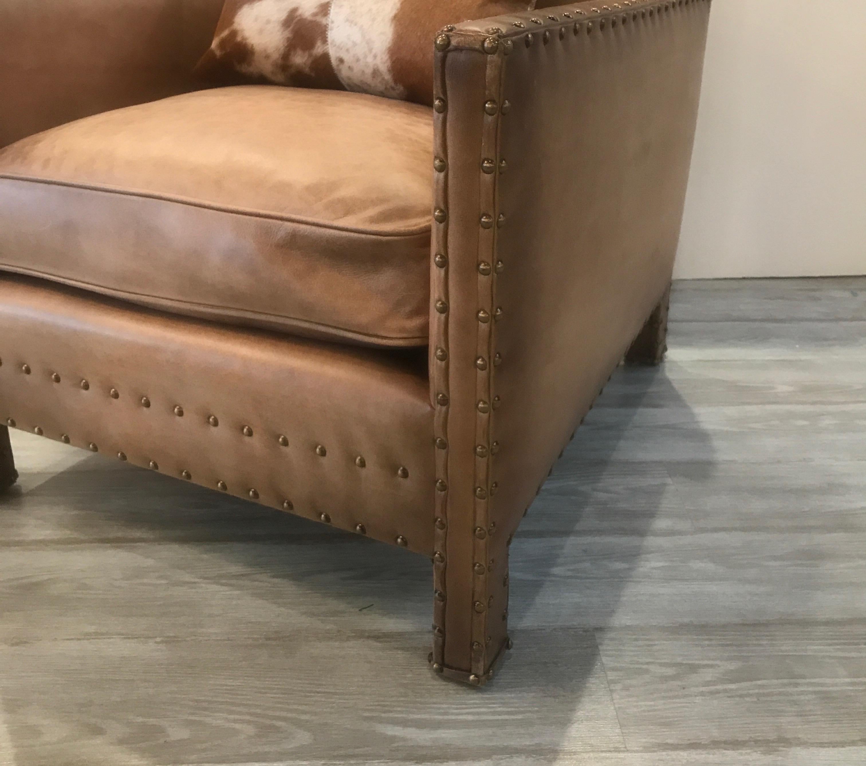 Ralph Lauren leather and brass nail head trim club chair. The solid walnut frame with 8 way hand tied hourglass coil construction covered in a tan colored leather with a slight intentional fading. The chair with a beautiful cowhide accent pillow.