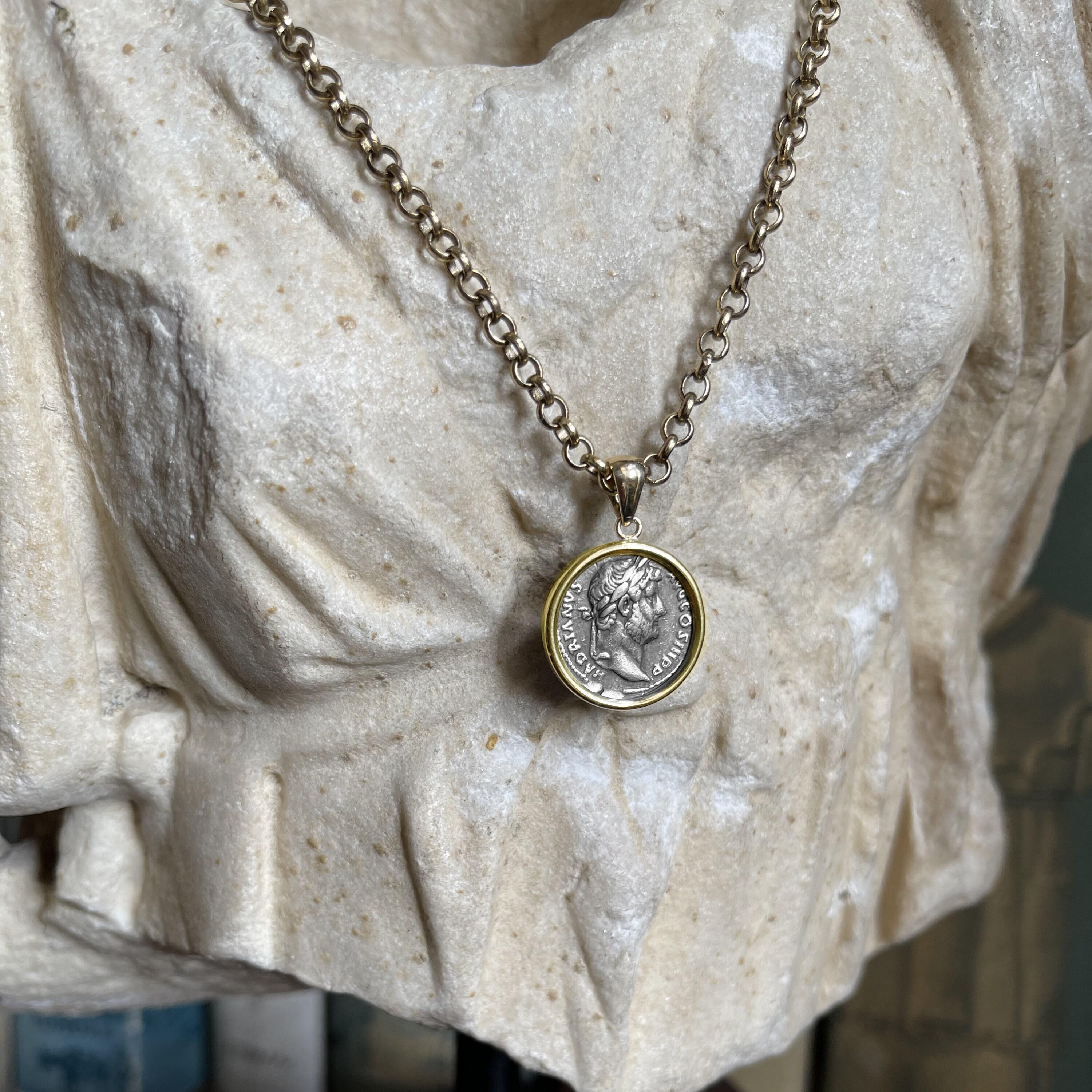 This exquisite 18 Kt gold pendant showcases an authentic Roman coin from the 2nd century AD, featuring Emperor Hadrian on one side and the seated Goddess Fortuna on the other. Hadrian, celebrated for his extensive travels and ambitious building
