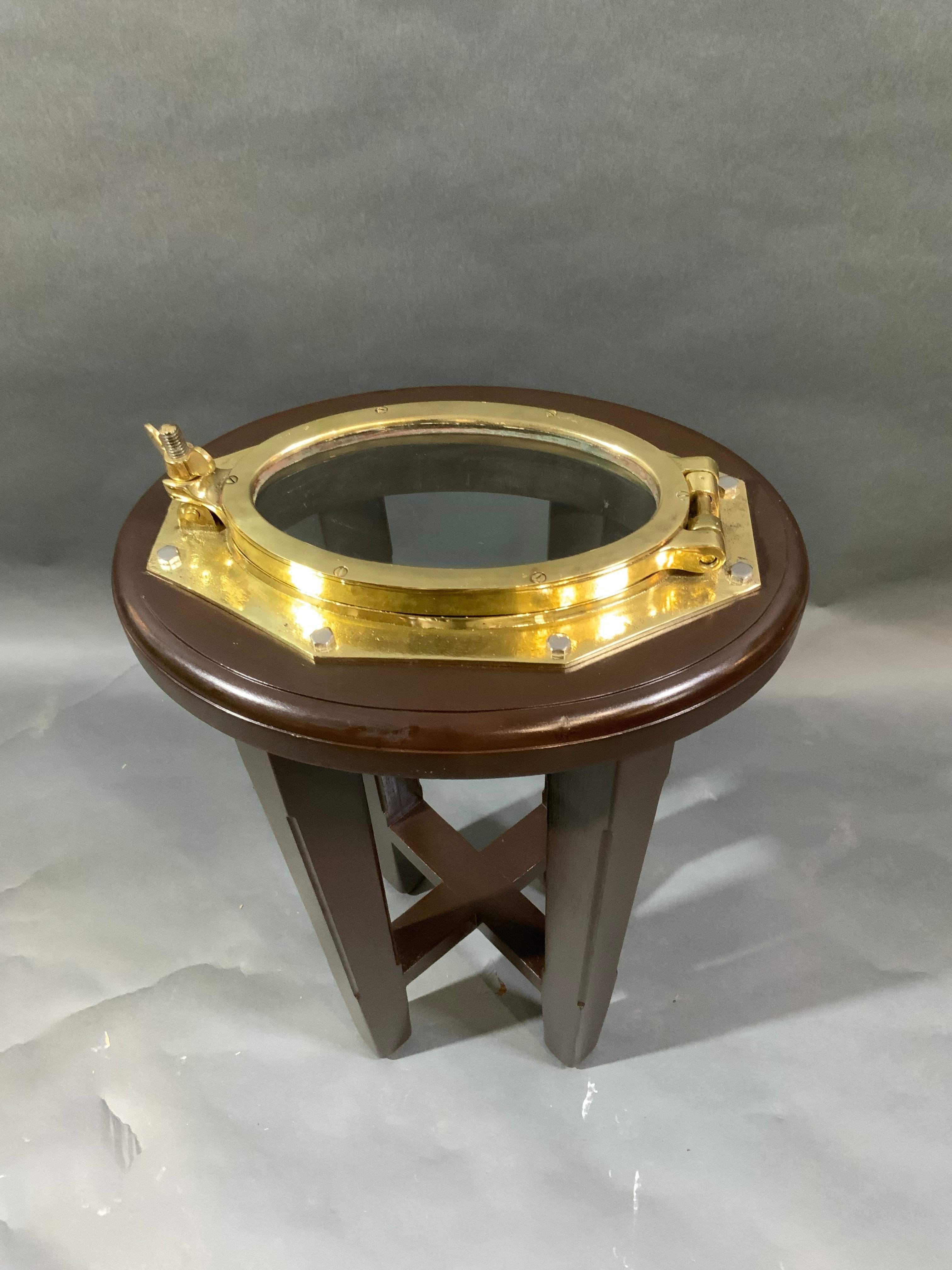 Solid brass highly polished and lacquered yacht or boat porthole fitted to a mahogany side table. This has been meticulously polished and lacquered and this is a great old relic. Weight is 14 pounds. Dimensions are 24 tall with a 15 by 11 inch top.