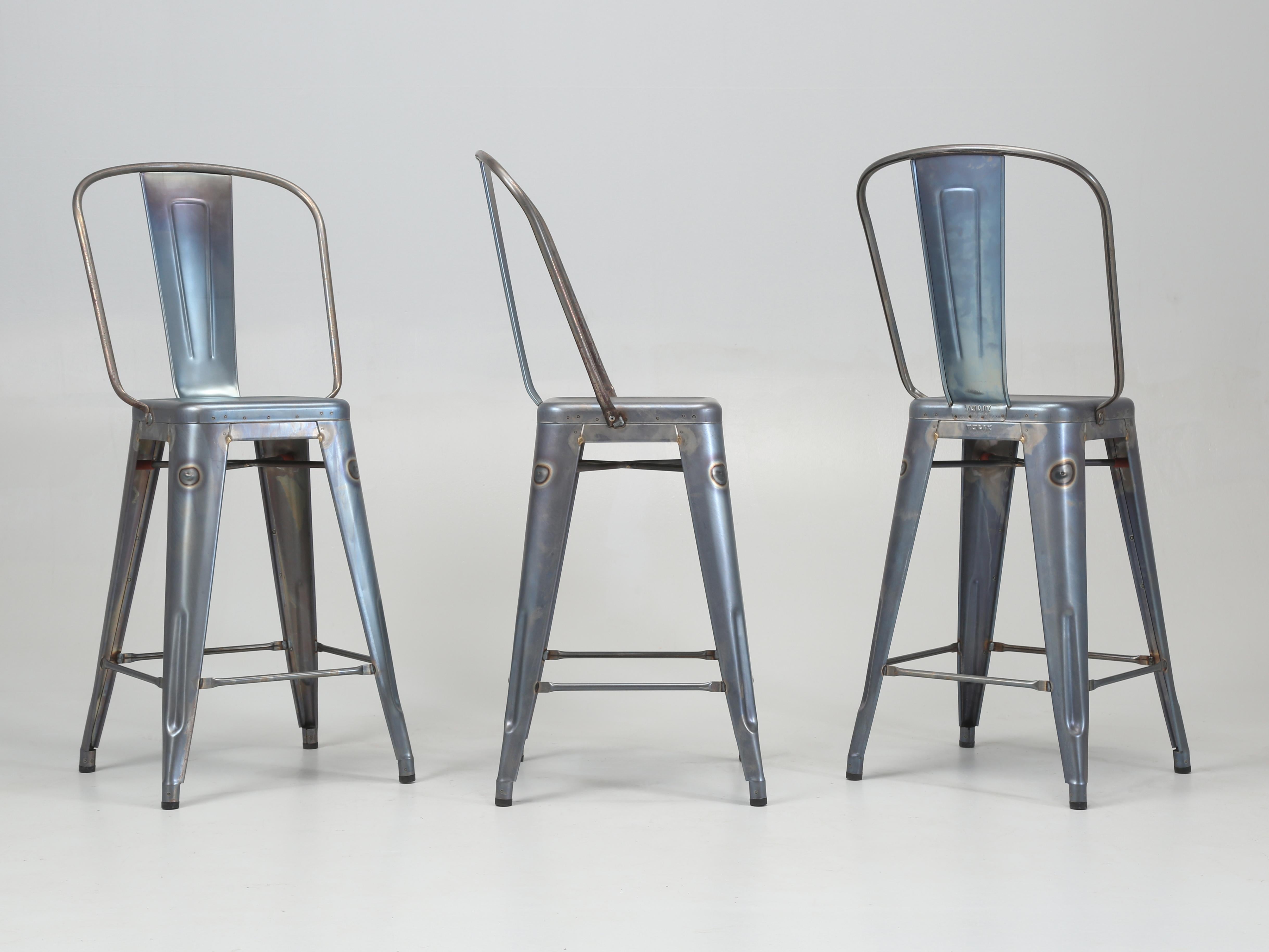 Auténticos taburetes altos de acero de fabricación francesa en un lavado azul sobre metal en bruto. Actualmente tenemos en stock algo menos de 900 piezas de auténticas sillas de comedor, taburetes de barra, taburetes de bar y taburetes de mesa Tolix
