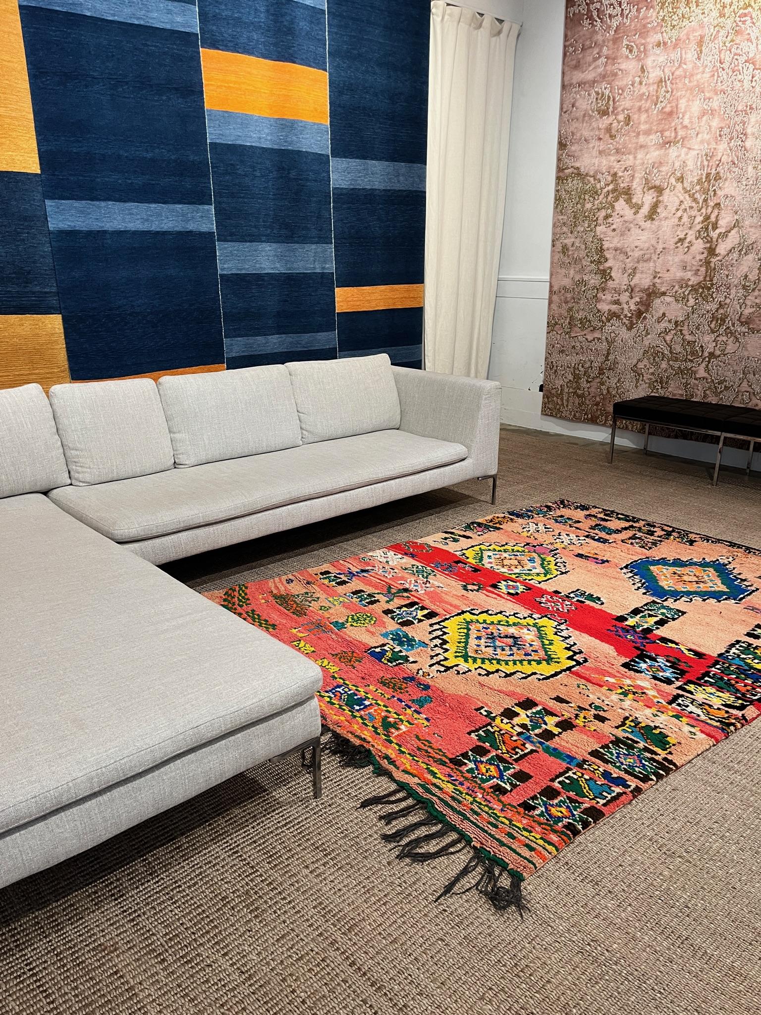 Una rara alfombra marroquí vintage de colección de los años 80 o 90. Se trata de un ejemplar encantador y juguetón, con colores muy vivos. Con un bonito tinte de fondo rosa con una franja roja y adornos azules, amarillos, verdes, blancos y negros.