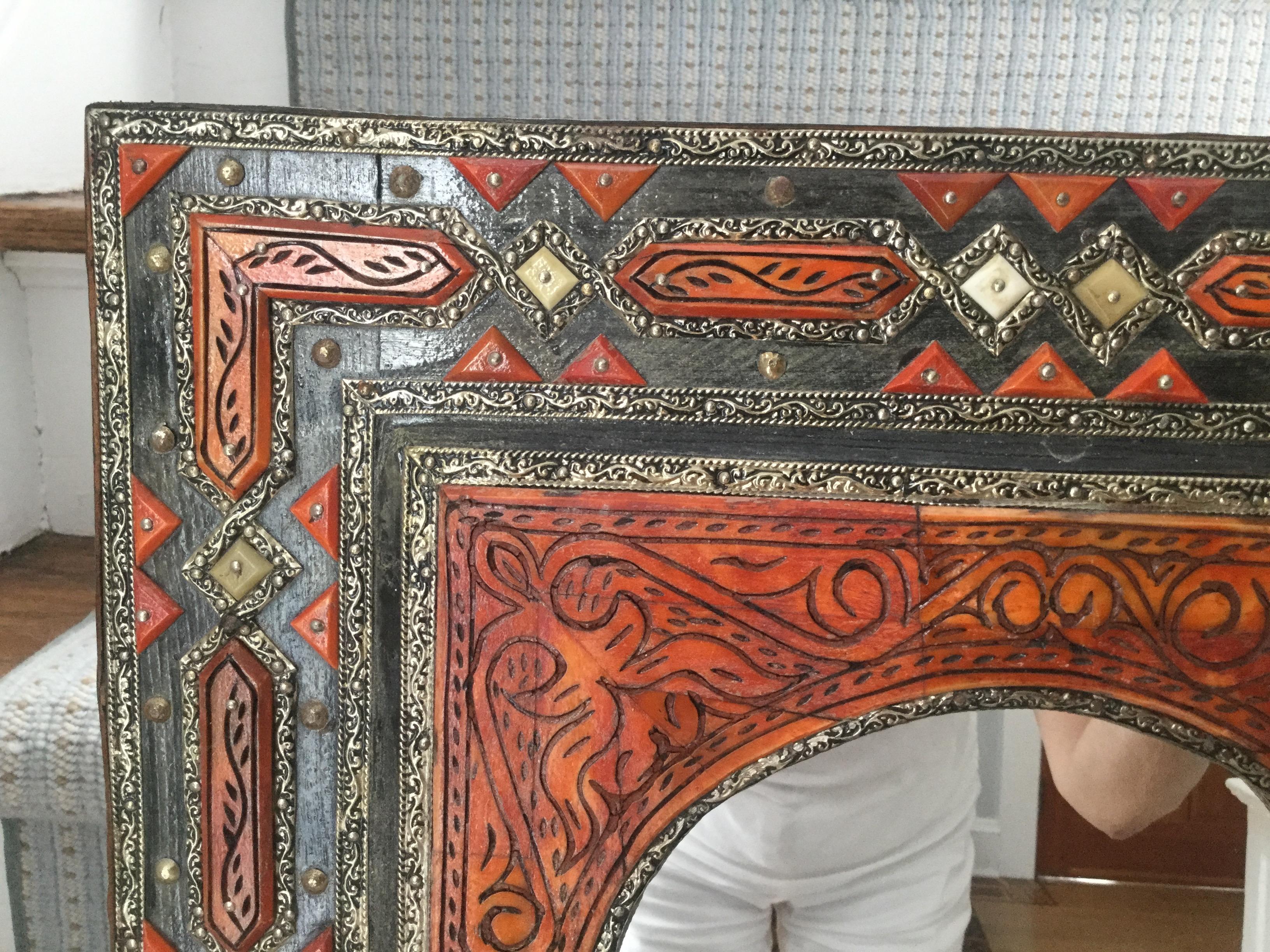 This stunning Moroccan mirror is made of solid wood with bone and silver overlay and has a painted orange wash with black scroll work and geometric pieces of bone with silver throughout the frame. The back is covered in brown cow-hide.



    