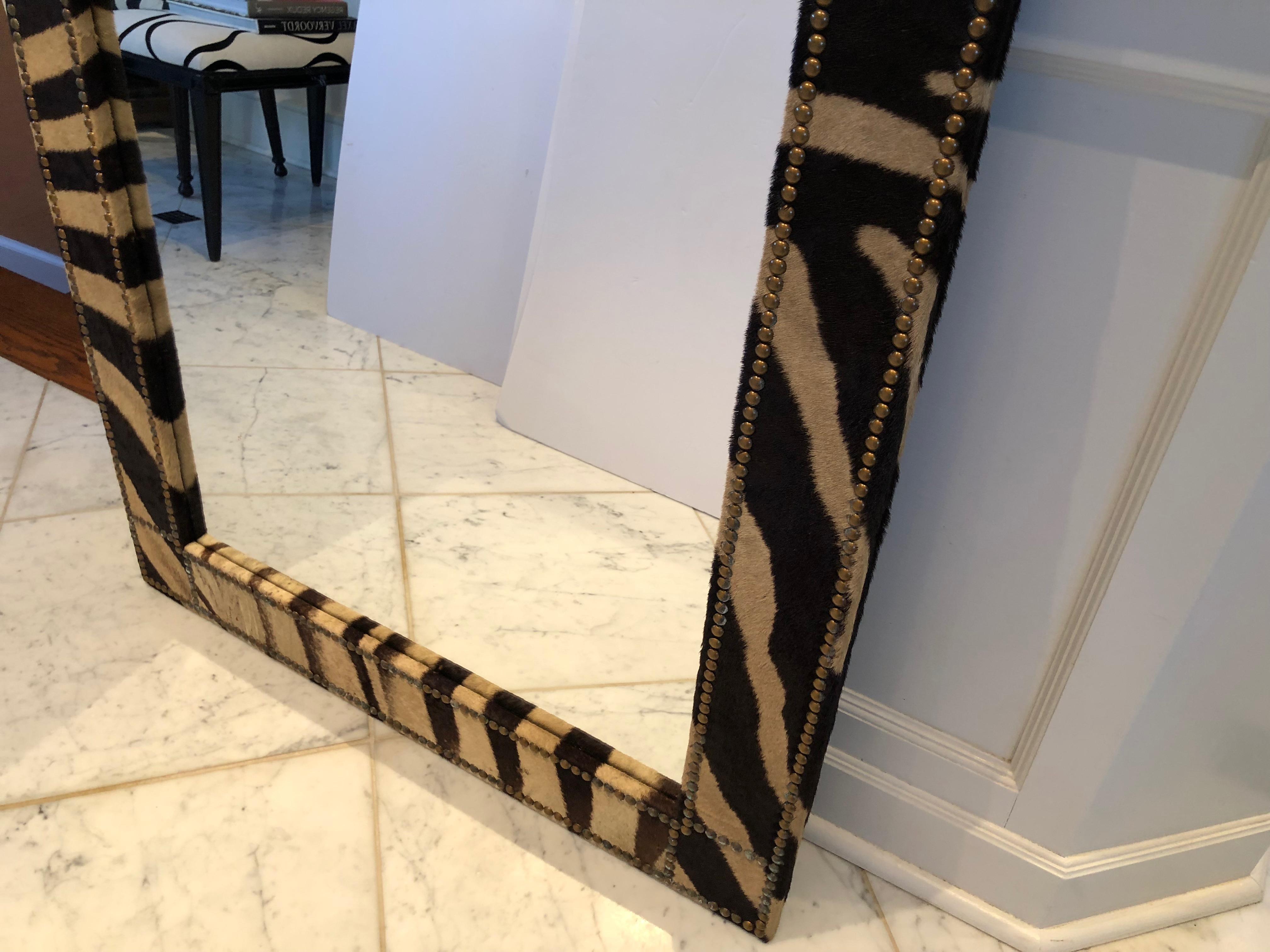 Super chic custom made mirror upholstered in zebra hide and finished with French antique brass nailheads. A pair is available.