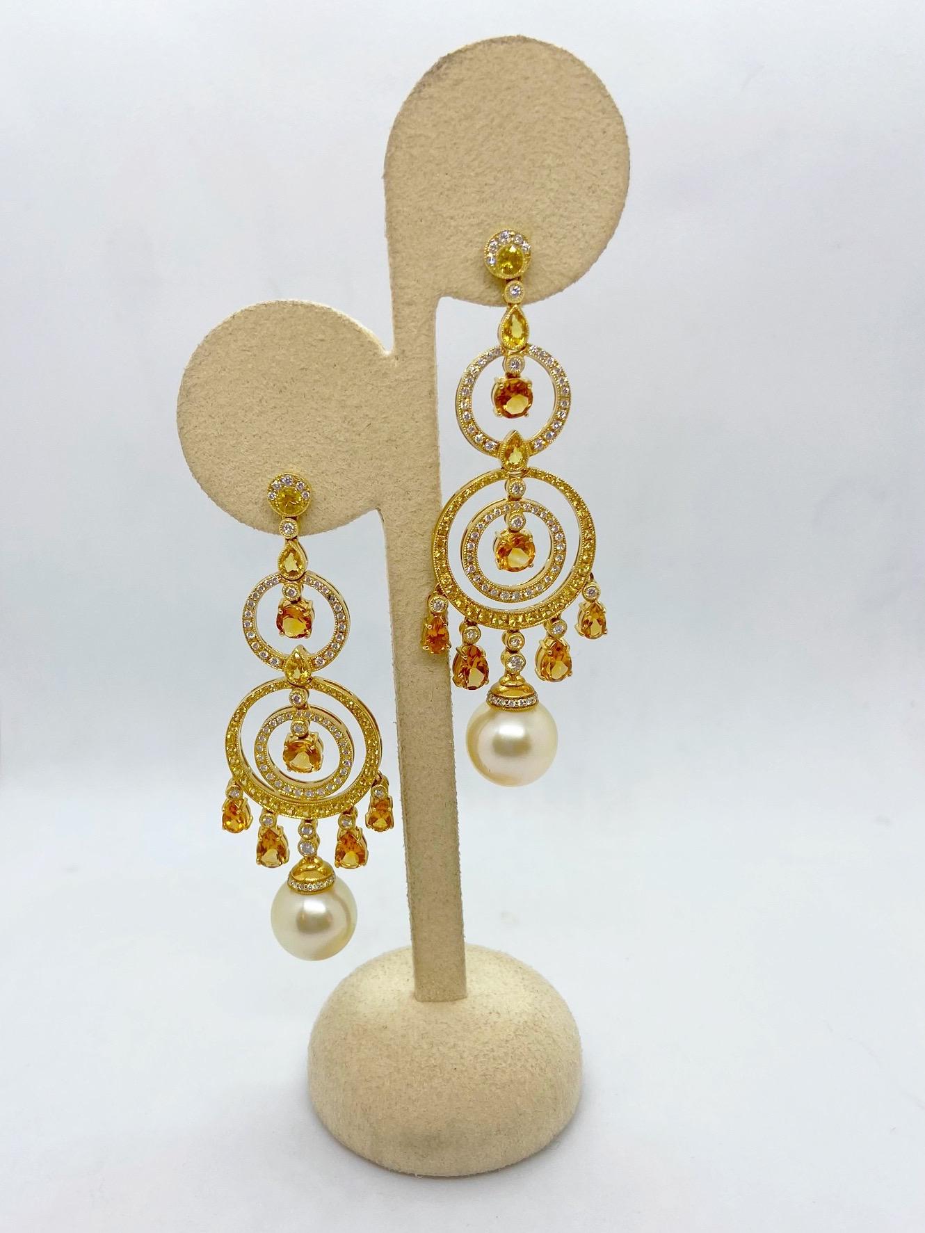 A beautiful pair of 18 karat yellow gold hanging earrings designed with rings of Yellow Sapphires. Pear shaped and round faceted Citrines dangle from bezel set Diamonds. 12mm Golden Pearls hang from the bottom.
The earrings have post backs and are 2