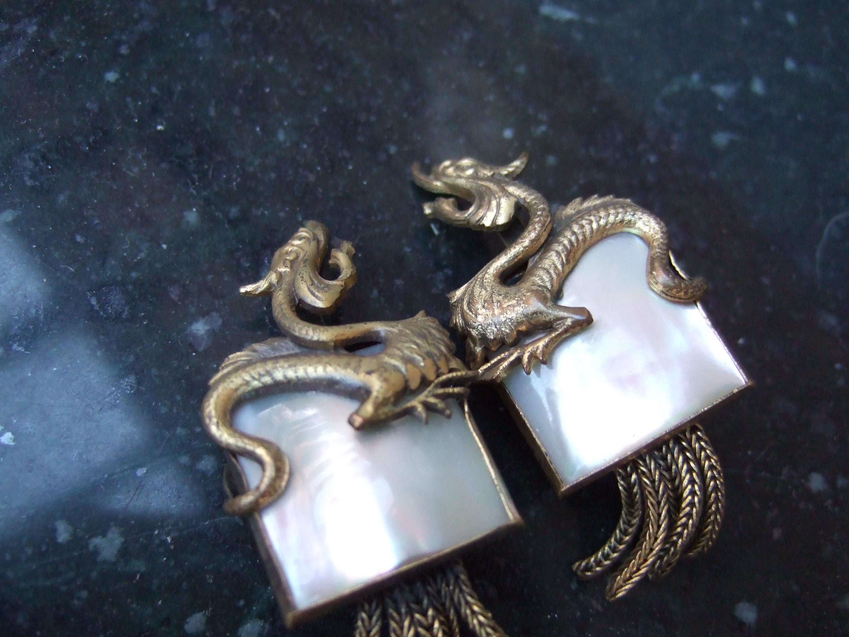 Avant-garde brass mother of pearl dragon design clip-on earrings c 1960
The unique mid-century clip-on earrings are designed with a pair
of stylized mythical dragons in brass tone metal 

The center of the earrings are embellished with a square