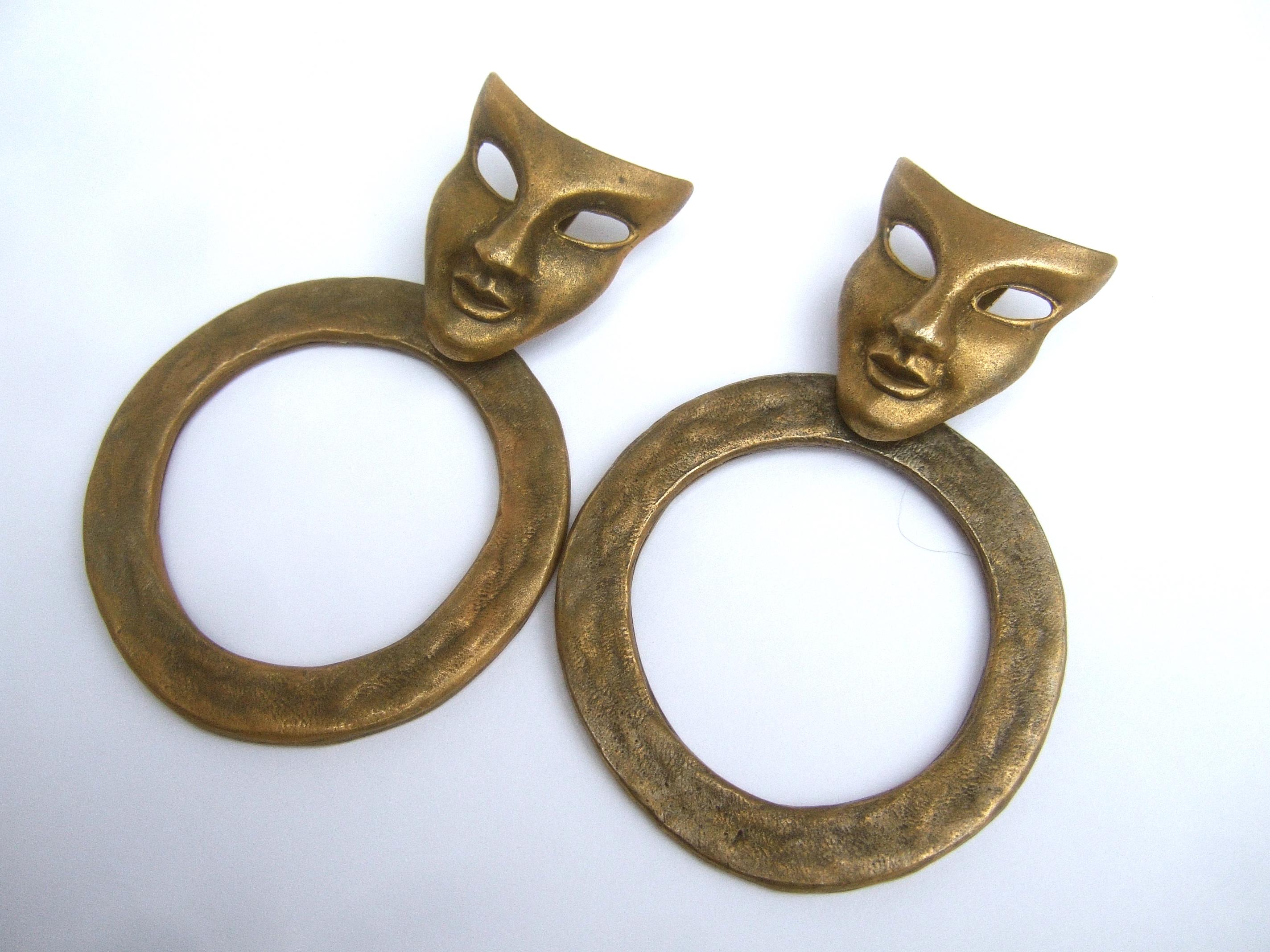 Avant-garde large-scale clip-on statement earrings designed by Les Bernard c 1980s
The unique large-scale earrings are designed with an androgynous mask; paired with an articulated circular flattened hoop ring; suspended underneath the chin 

The
