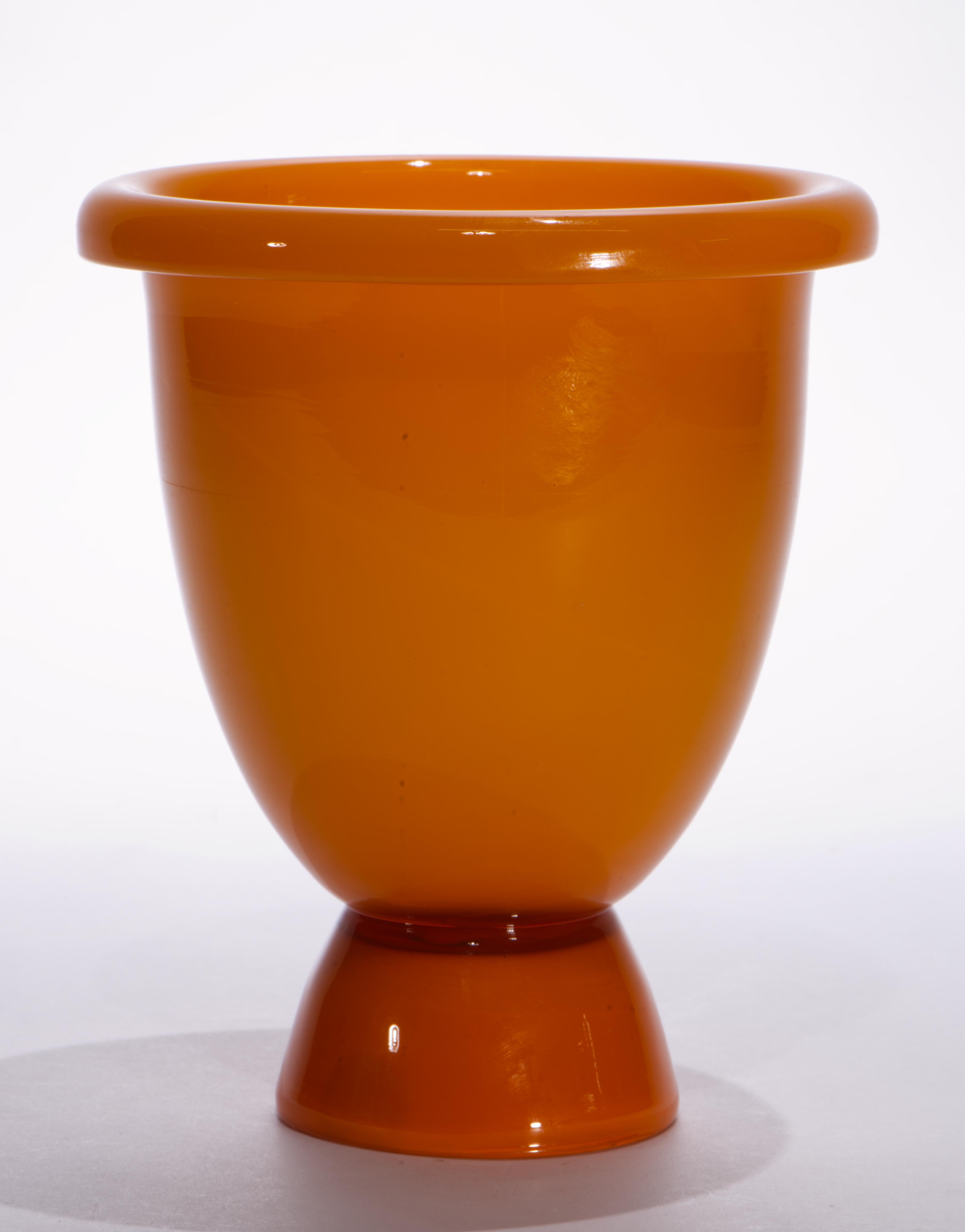 L'insolito vaso d'epoca in vetro di Murano è caratterizzato da una forma a ciotola con piede affusolato e bordo arrotolato; il piede conico fuso è visivamente separato dal resto del vaso da uno strato di vetro arancione semitrasparente che racchiude