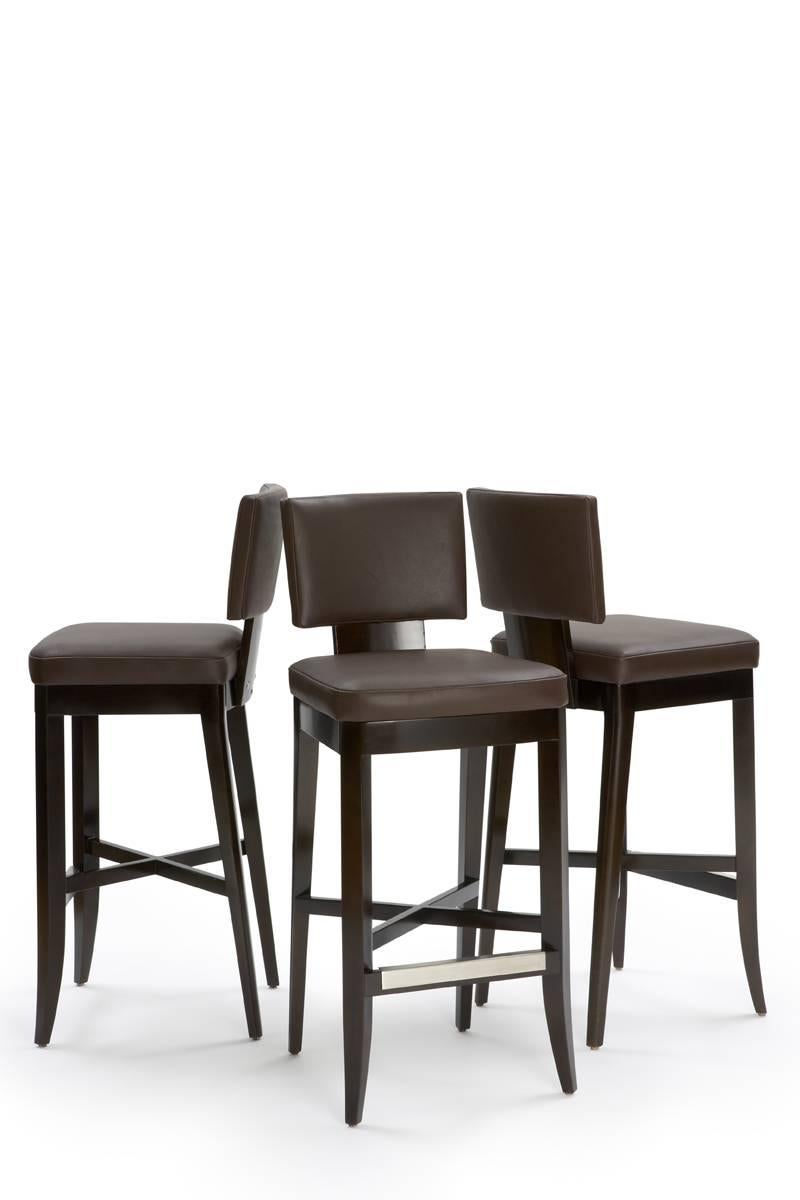 Counter height stool in dark wood finish with wood-framed upholstered seat and curved upholstered back. Double-stitched seams. Foot guard in brushed stainless steel. Measures: Seat height approximately 26