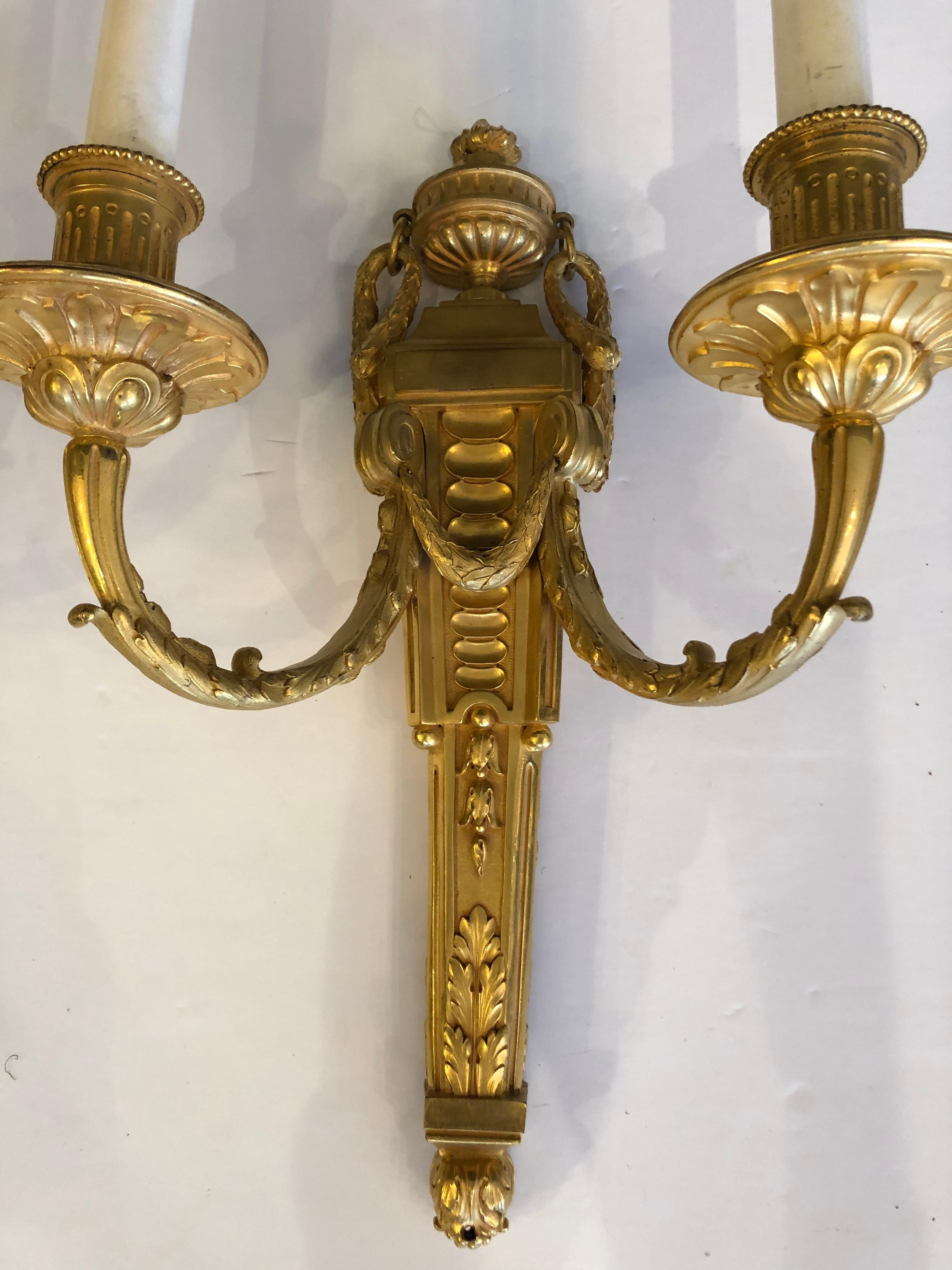 A gorgeous heavy doré gilt bronze pair of neoclassical style electrified wall sconces by Caldwell having two arms and incredible decoration.