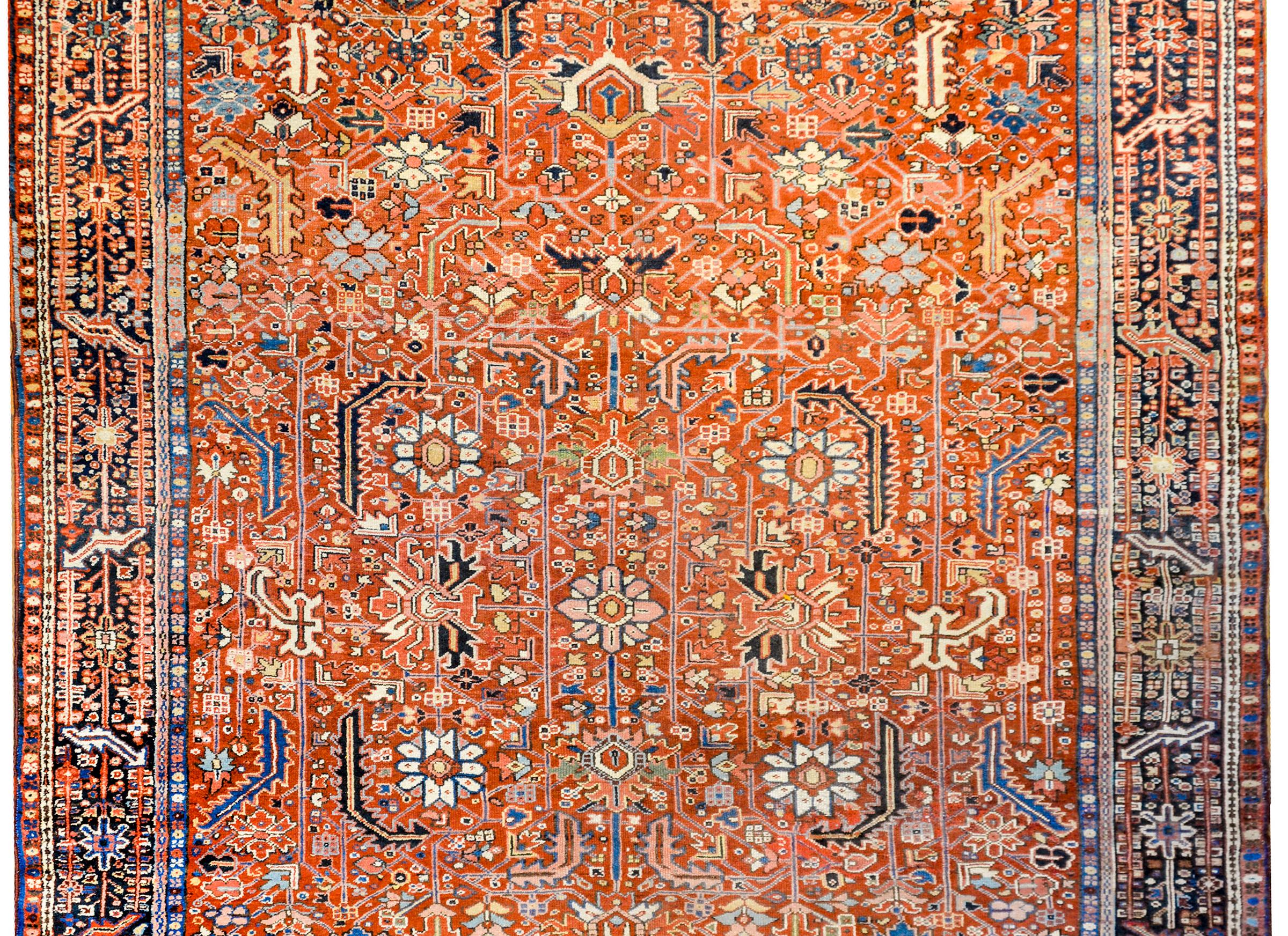 An awesome early 20th century Persian Heriz rug with an all-over myriad floral and leaf pattern rendered in gold, indigo, white, black, green, pink, on a bold crimson background. The border is exquisite with a wide dark indigo stripe with a densely