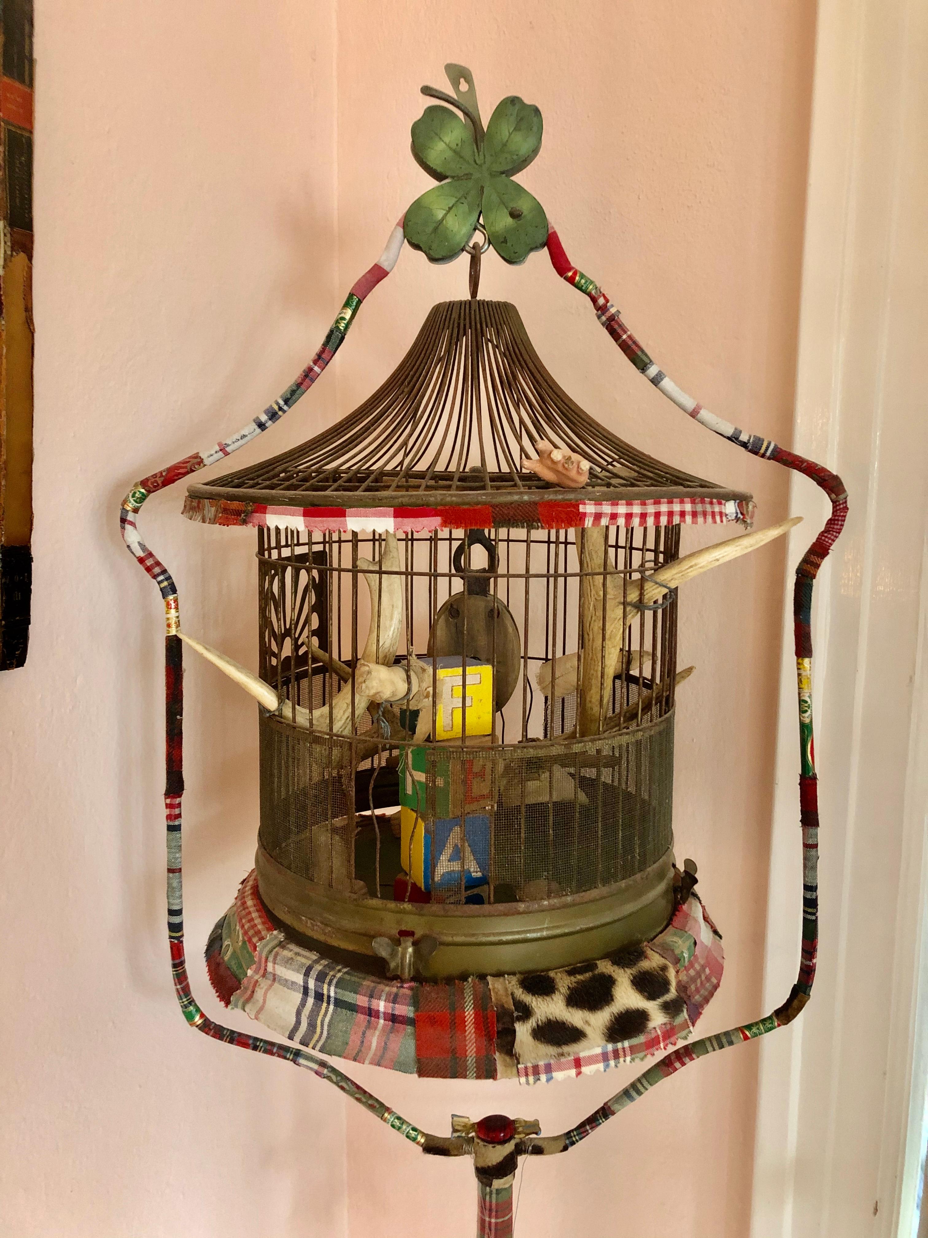 A beautiful and thoughtful found object sculpture titled Cage of Fear made from a vintage birdcage collaged with gingham, leopard fabric and cigar box wrappings. Inside the cage is a 3 dimensional arrangement of mixed-media objects including