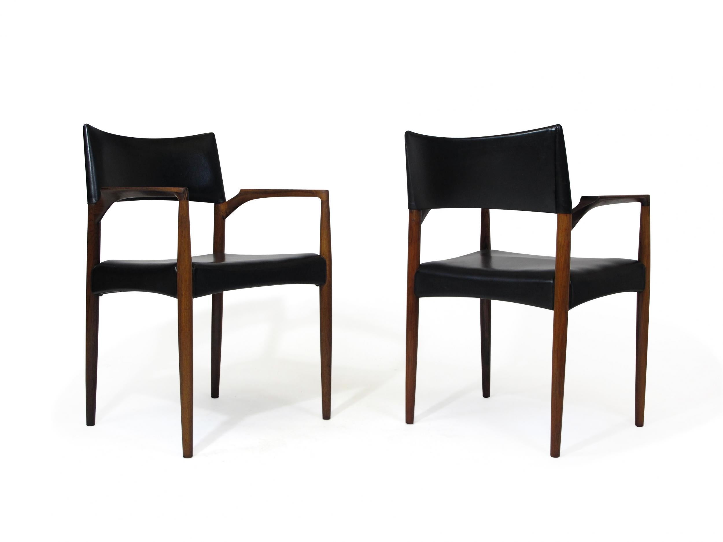 Aksel Bender Madsen dining armchairs crafted of solid Brazilian rosewood with sculpted arms and a comfortable backrest. The pair of chairs are in their original finish and upholstered in the original black vinyl. 
 