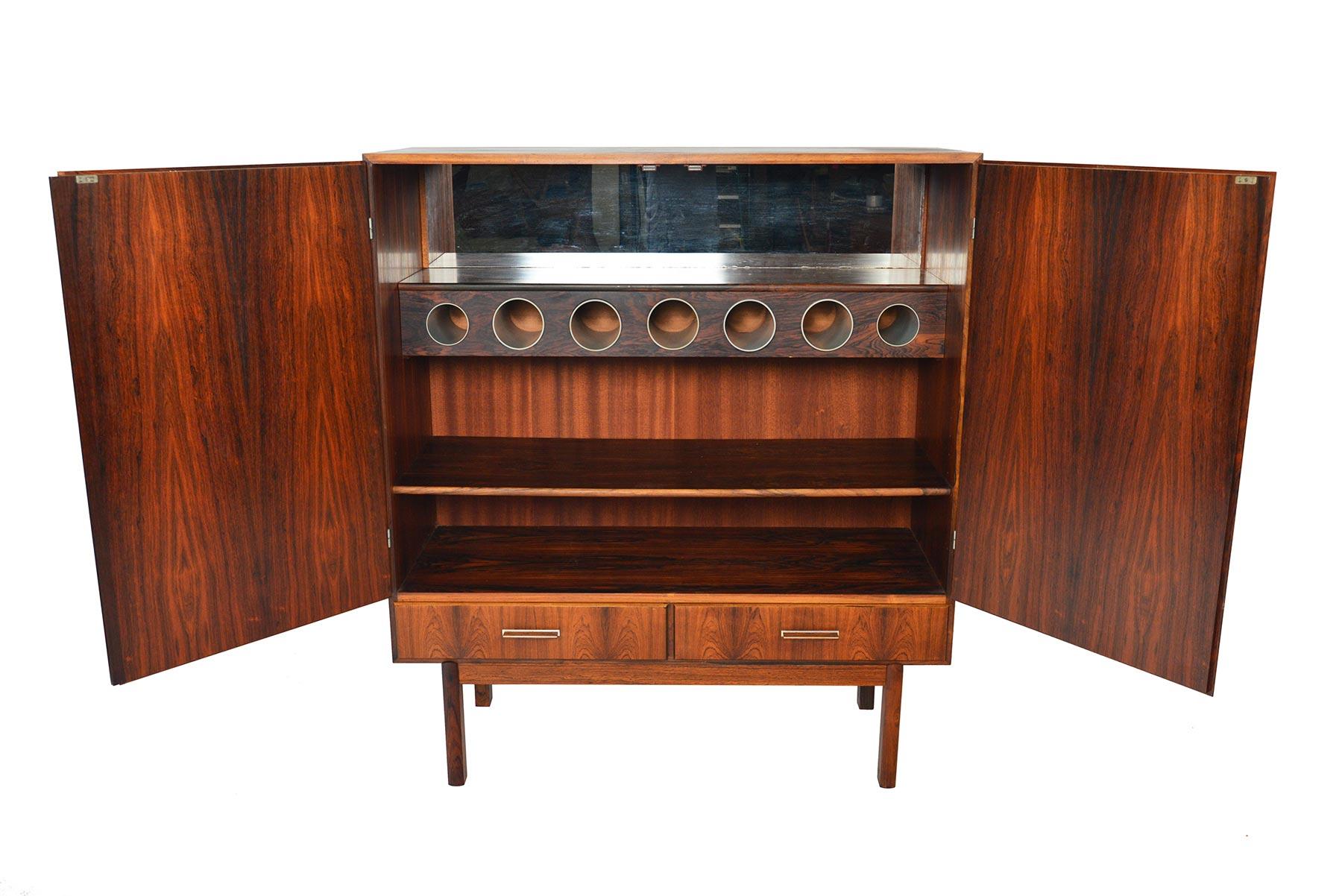 This large dry bar by Axel Christiansen Odder offers an impressive amount of storage and drama! Crafted in bookmatched Brazilian rosewood with aluminum handles, two large doors open to reveal a mirror lined interior, bottle storage, and an