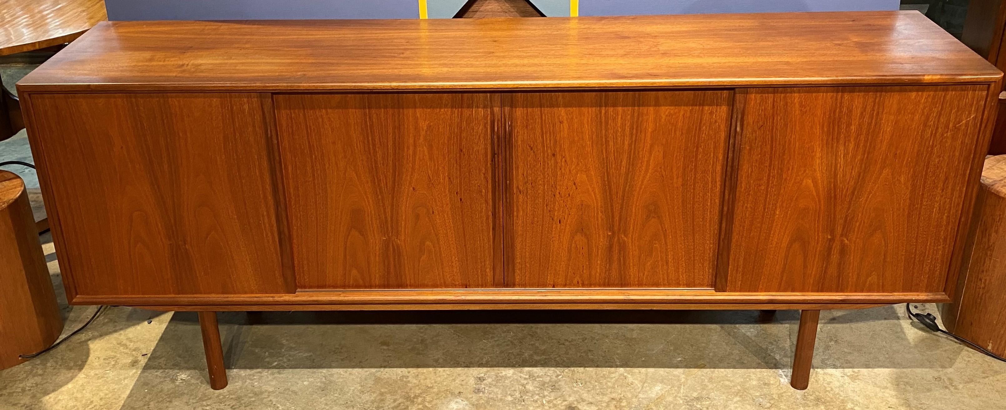 A fine example of a sleak designed Mid-Century Modern Danish teak credenza designed by Axel Christensen Odder, with four front track sliding doors, one of which opens to three felt lined drawers, and the other three open to a single interior storage