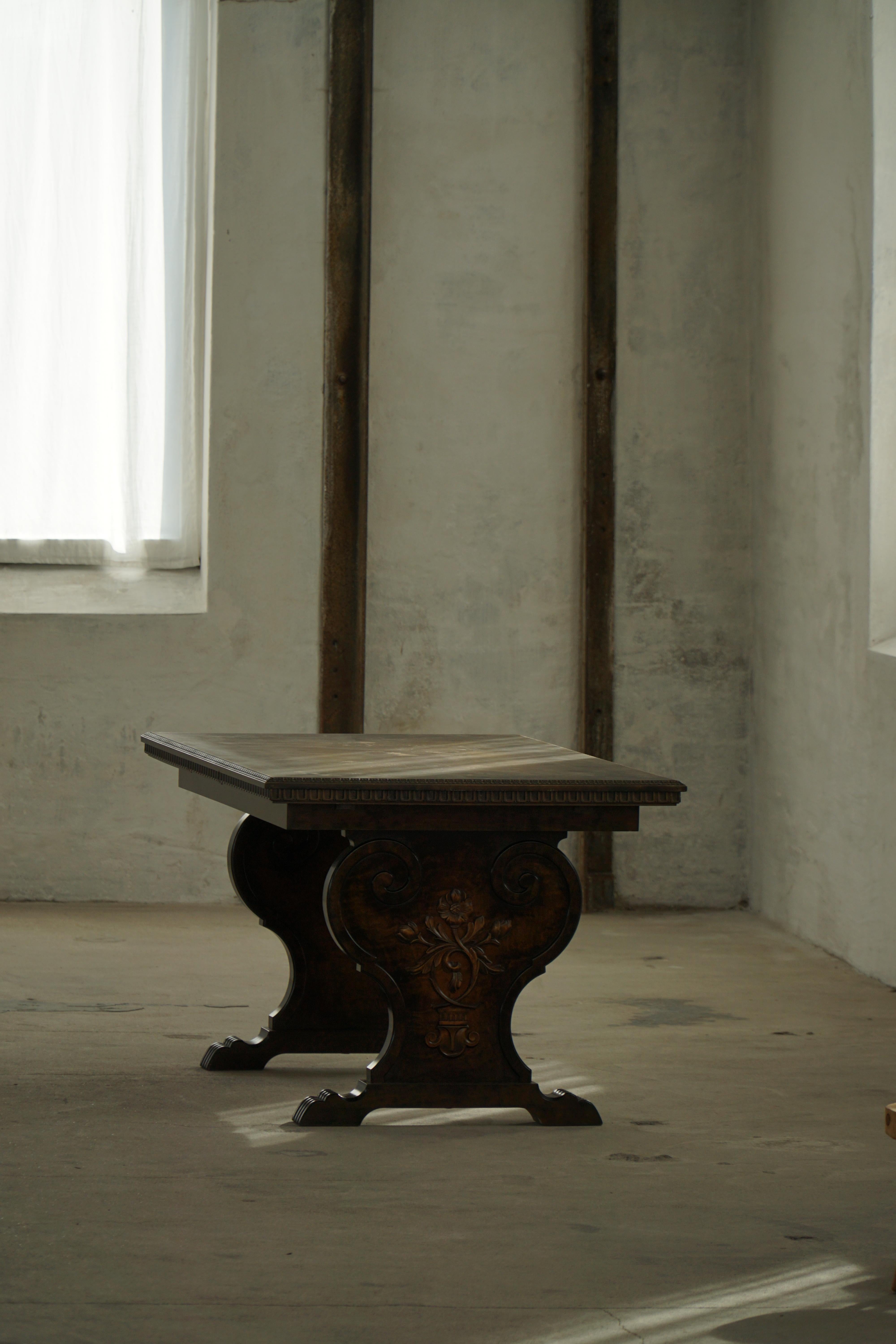 An extravagant Swedish Grace dining table from the early 20th century, crafted in dark birch veneer with finely carved details. The table features a richly decorated apron and legs with carved motifs, rounded and romantic forms, and a patinated