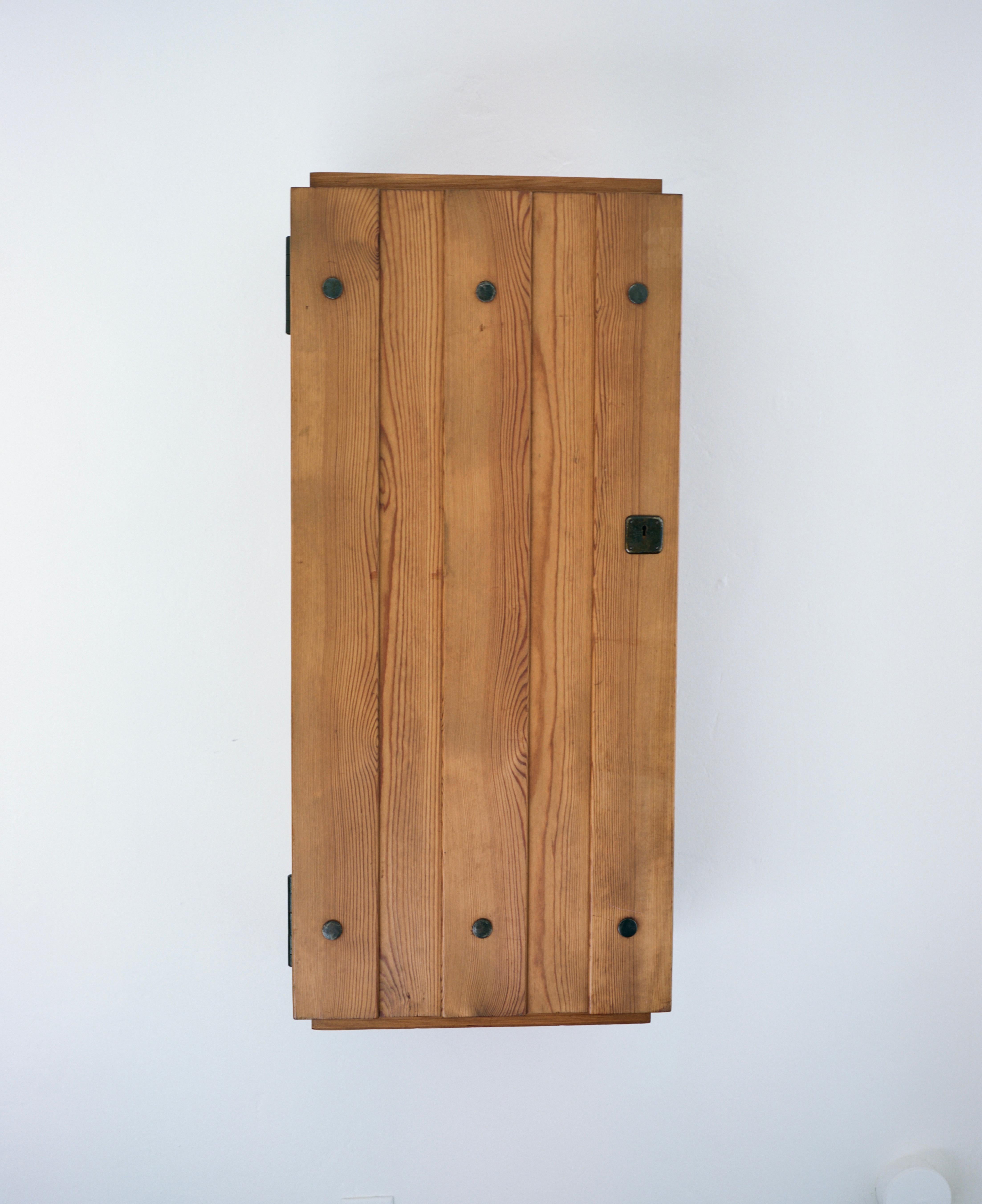 A pine wood wall-hanging cabinet by Axel Einar Hjorth from his “Sportstugemöbler” series designed for Nordiska Kompaniet. 
From 1926-1938, Axel Einar Hjorth was lead furniture designer of Sweden’s Nordiska Kompaniet department store and during that