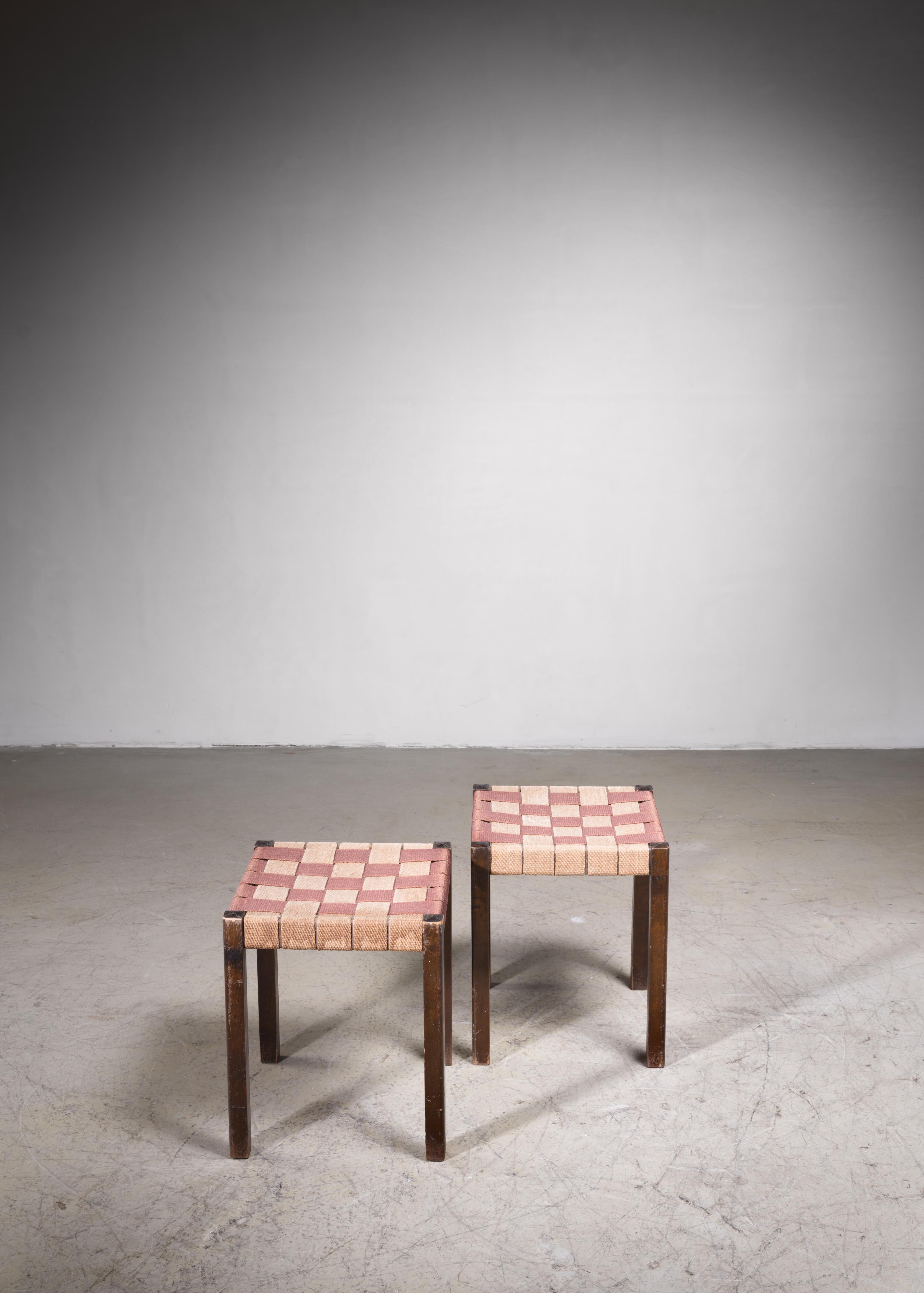 A pair of stools by Axel Larsson for Svenska Möbelfabriken, Bodafors, designed circa 1929. The stools are made of stained birch with a mixed red-brown and beige original canvas webbing. 

These pieces are in a good vintage and original condition.