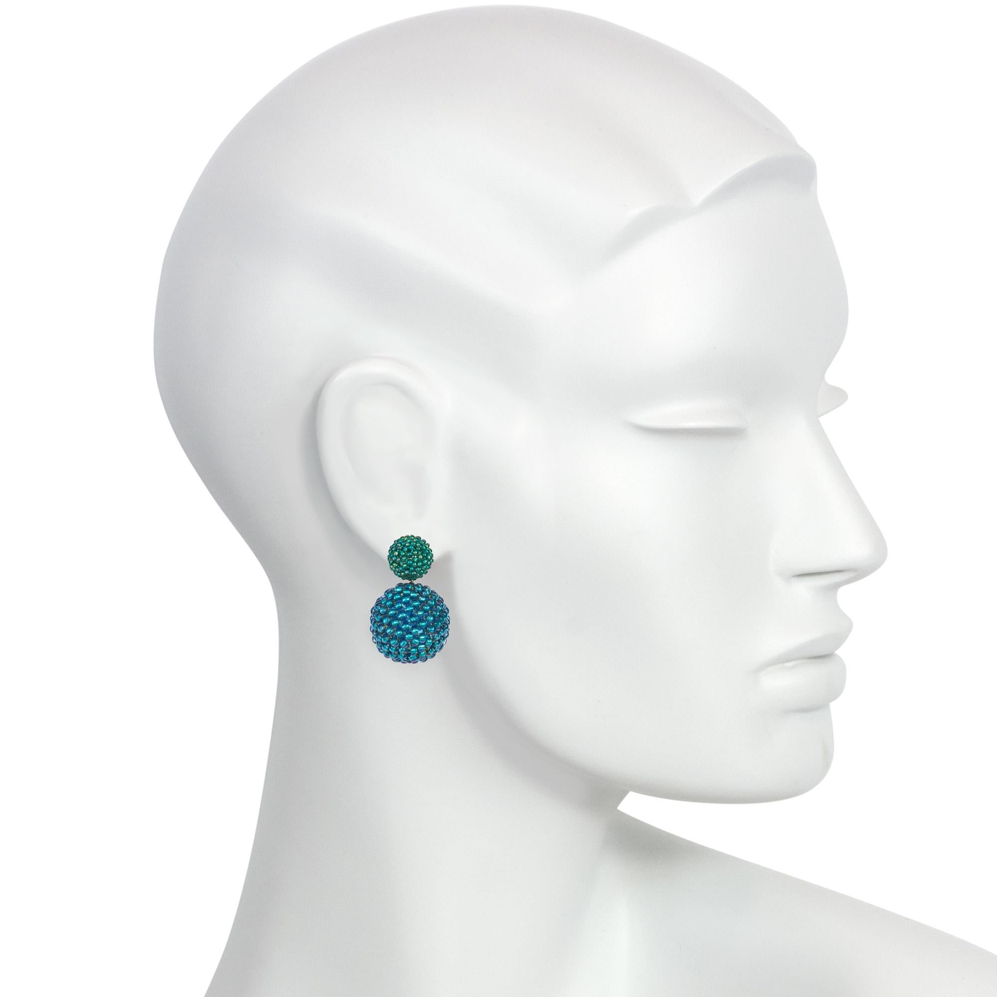 A pair of handmade double ball glass beaded earrings with matte iridescent green tops suspending larger spheres of 