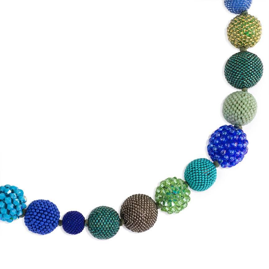 A hand beaded ball necklace comprising 28 glass and crystal beaded spheres of varying sizes in white, blue, grey, turquoise, teal, green, and gold tones, completed by an 18k gold hidden clasp.  Axel Russmeyer
Beads measure approximately 13-22.5mm