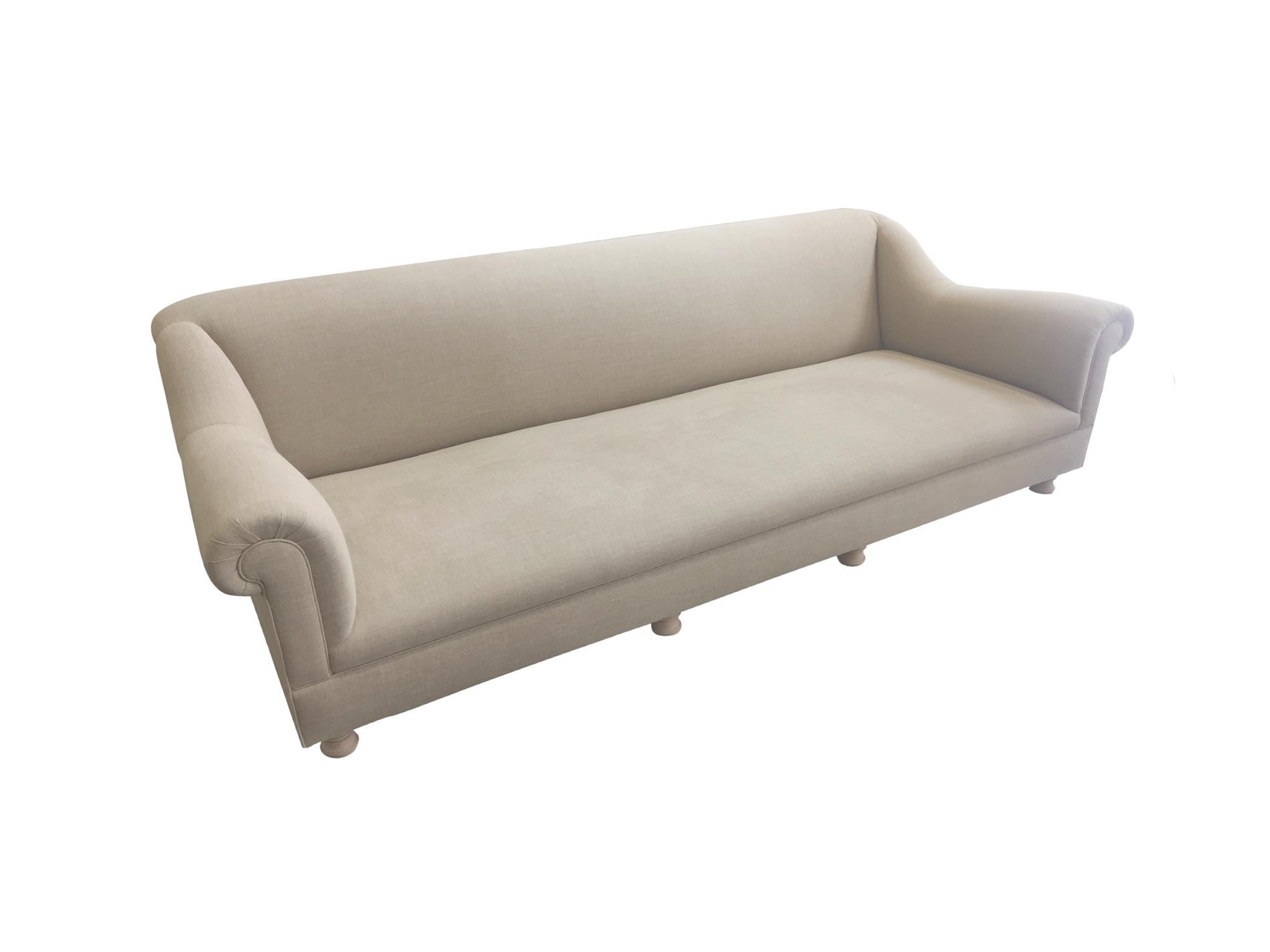 An elegant, low sofa designed by the antiques dealer and interior designer Axel Vervoordt. The sofa is a modern take on classic forms. It consists of unadorned Belgian linen upholstery and unglazed wood bun feet. The austerity of the design brings