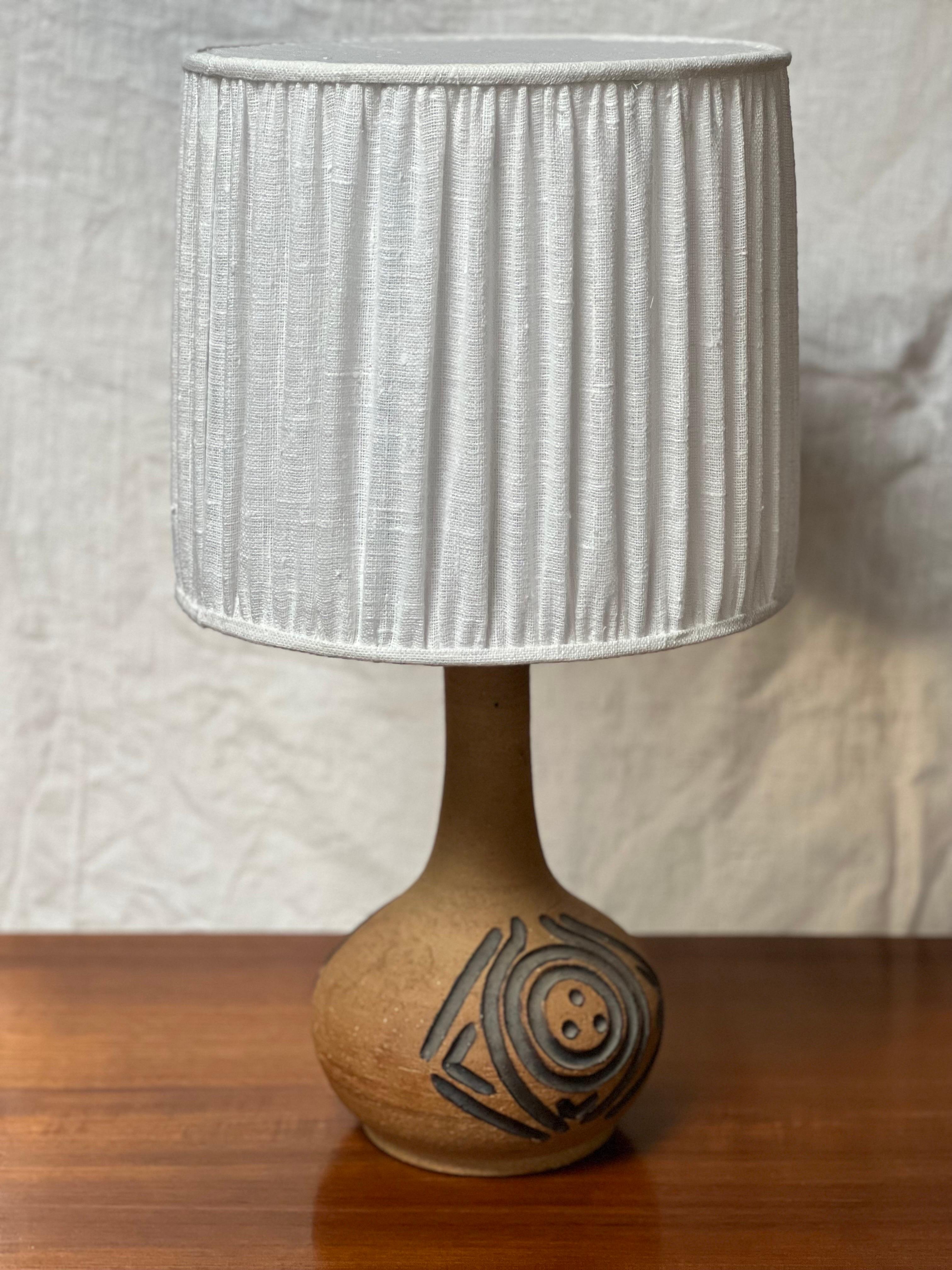 Die Lampe wurde in den 1970er Jahren im Axella Studio Design hergestellt, einer Keramikmanufaktur. Erdtöne mit stark geschwärztem Muster. Die Gesamthöhe dieser Lampe einschließlich des Schirms beträgt 57 cm. Der Schirm ist 27 cm hoch und hat einen