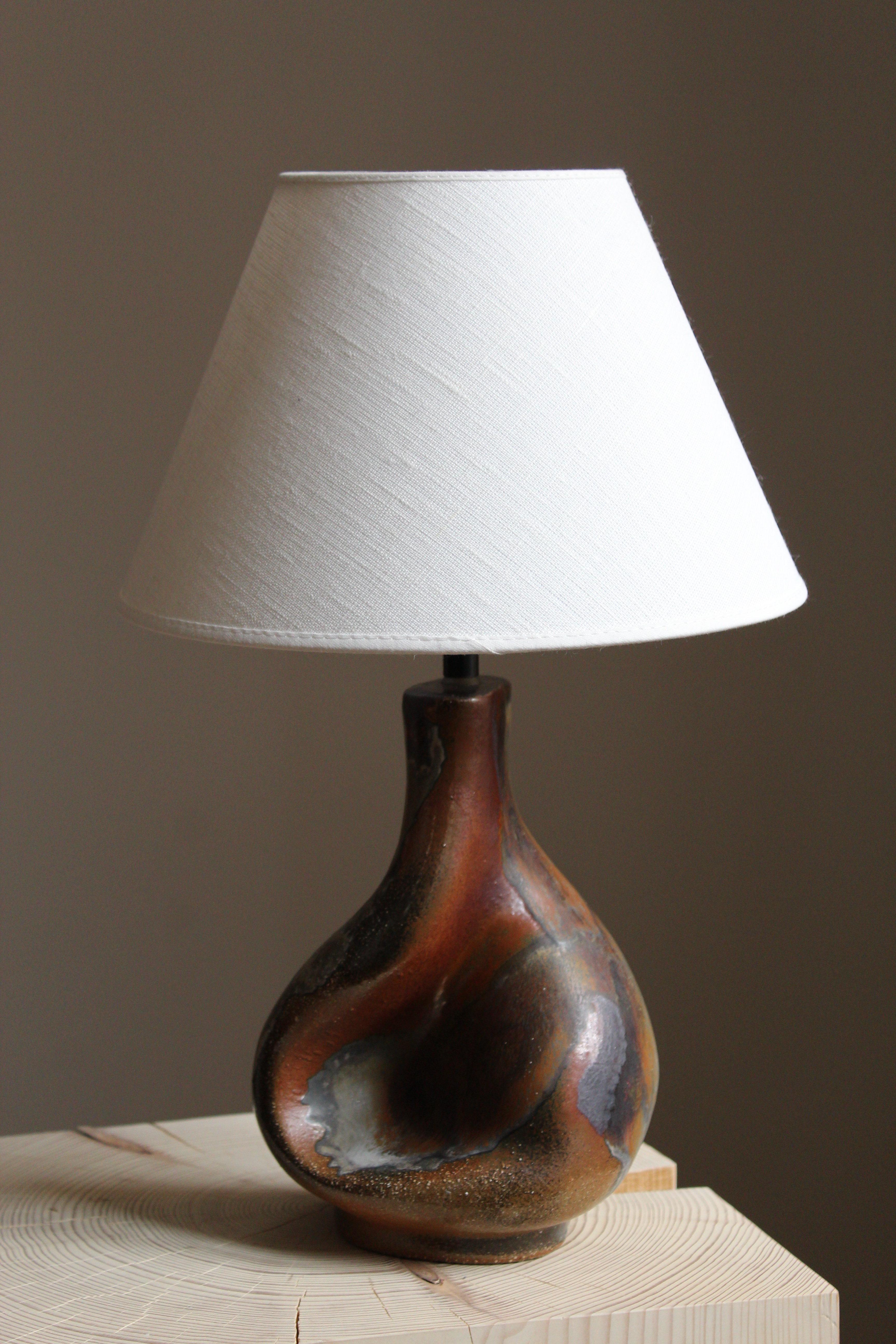 A table lamp produced and designed by Axella, Denmark, 1960s. With maker’s label.

Lampshade is attached for reference and are not included in the purchase. Measured without lampshade.

Glaze features brown-grey-dark colors.

Other ceramicists of