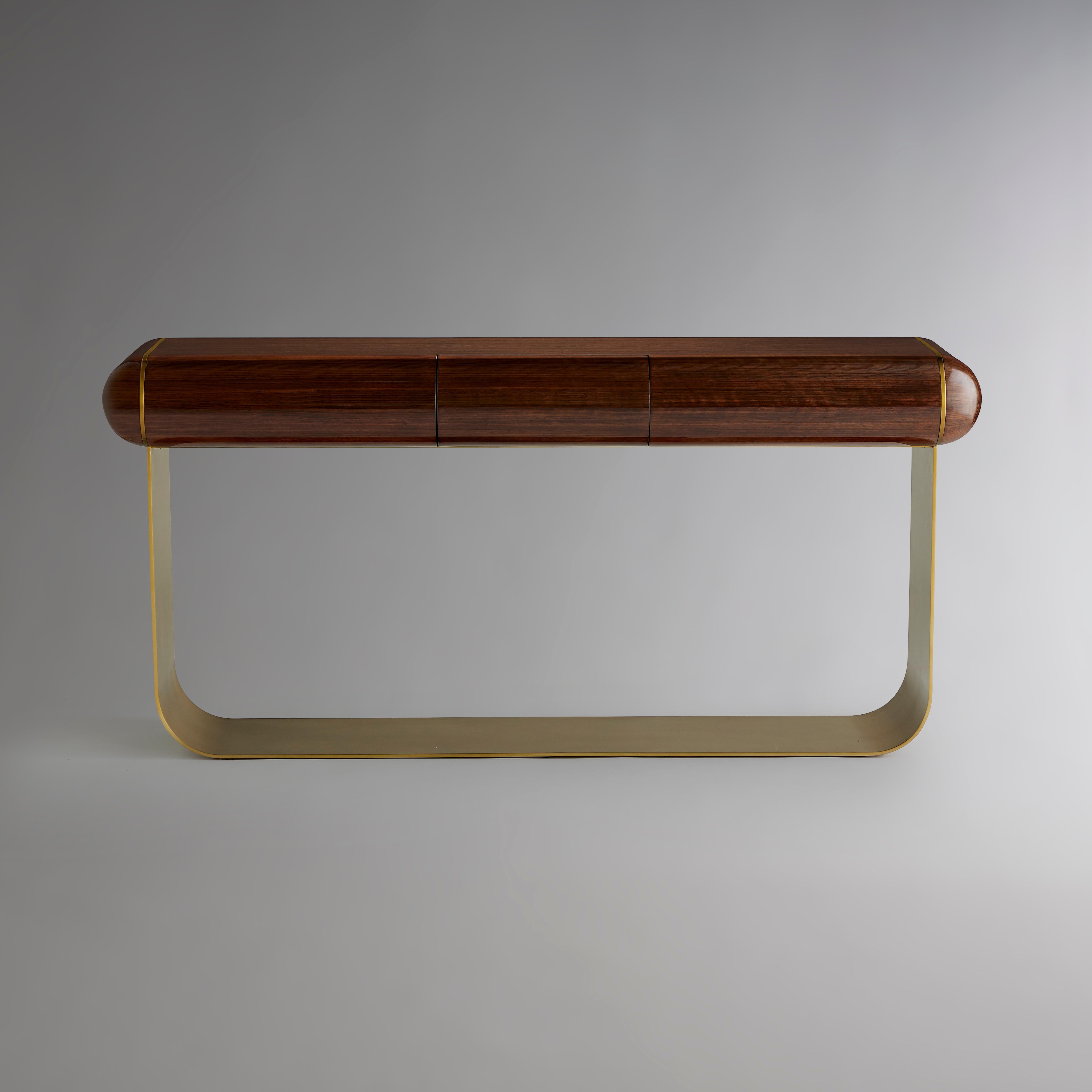 A seamless base of shaped brass anchors this refined console table with a top of high-sheen Daniella wood. Twin inlays of burnished brass on either end align with the vertical supports of the base. A central drawer offers subtle functionality for