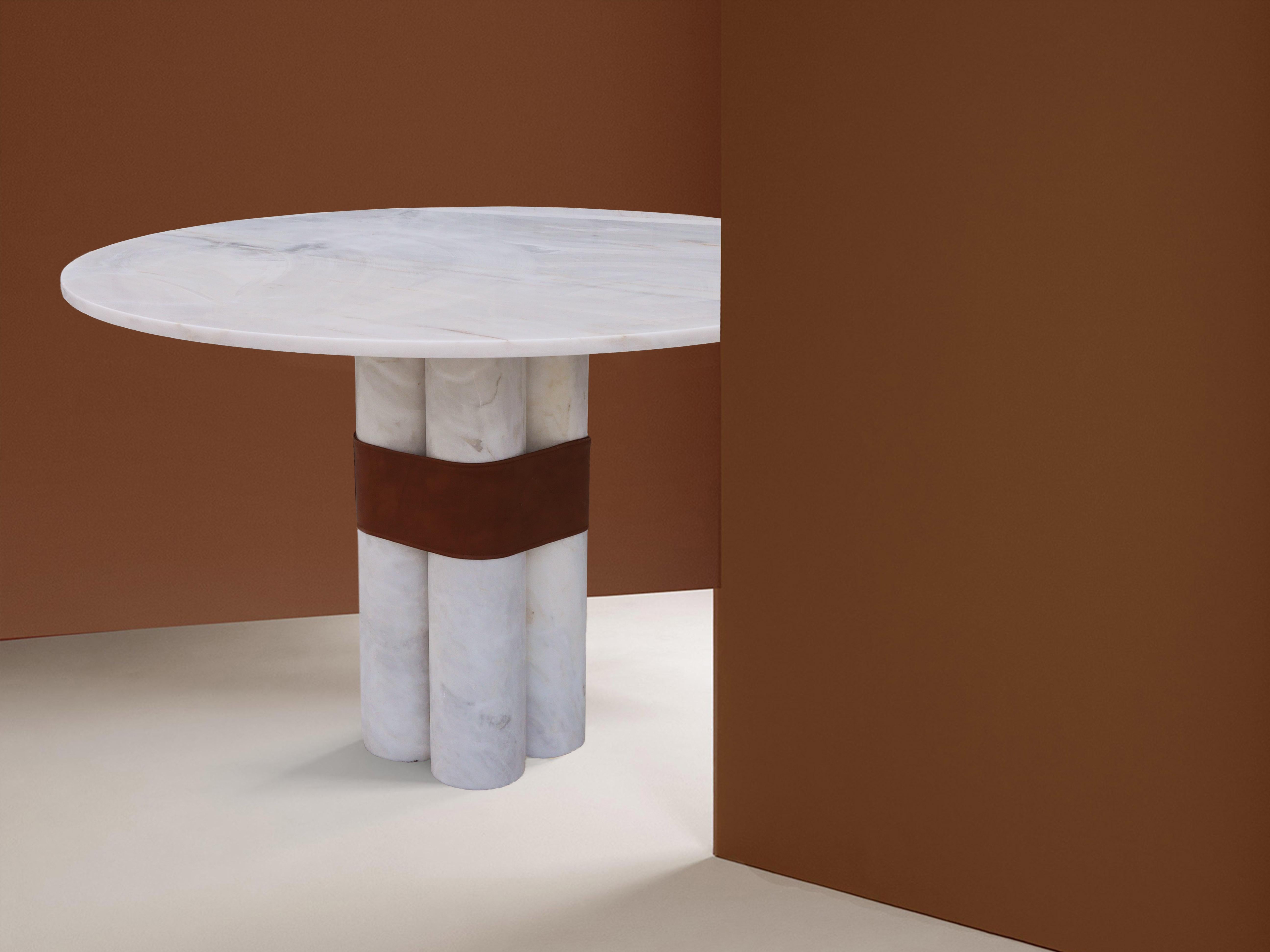 AXIS Runder Tisch 
Sein Sockel, der aus einem einzigen dünnen Block besteht, der an runde Säulen erinnert, und seine runde Spitze schaffen ein fast architektonisches Gleichgewicht. Der handgefertigte Öko-Ledergürtel, der die Struktur umschließt,