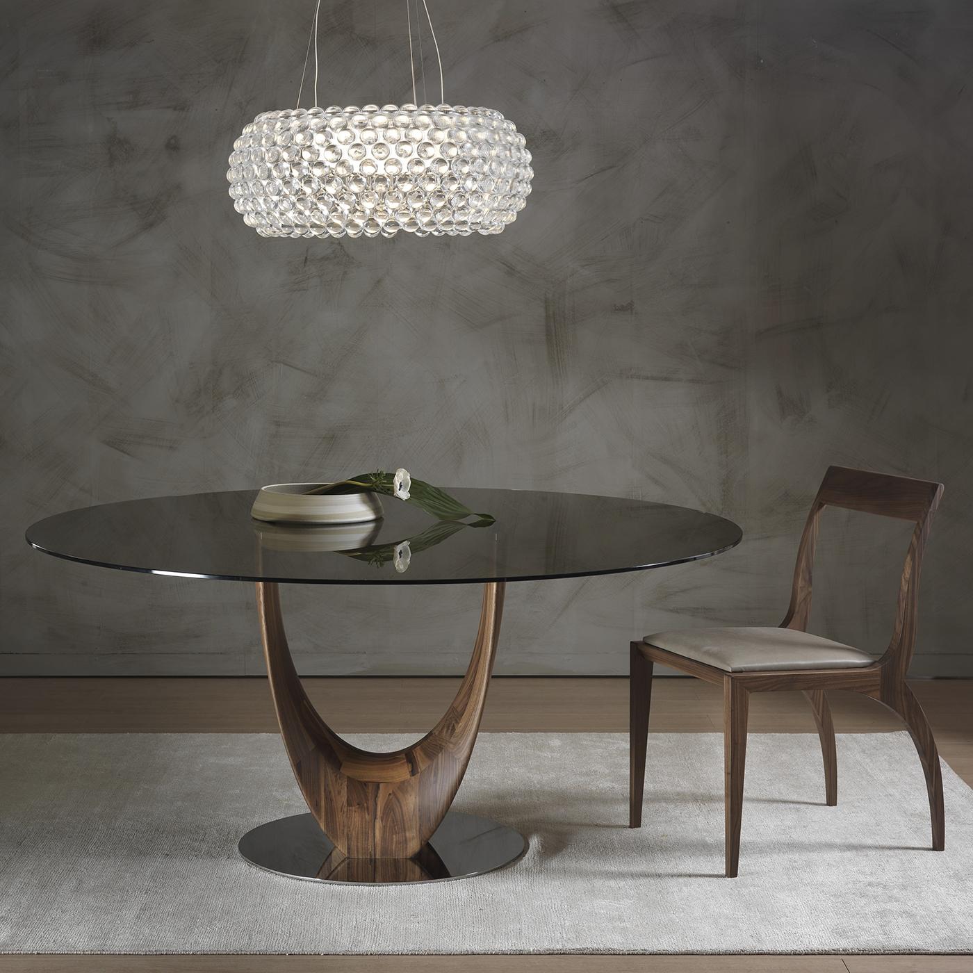 This elegant and modern dining table designed by Stefano Bigi features a stunning base in solid Canaletto walnut. The structure rests on a round element in chrome-plated metal and curves to form two separate legs that create a delicate sense of