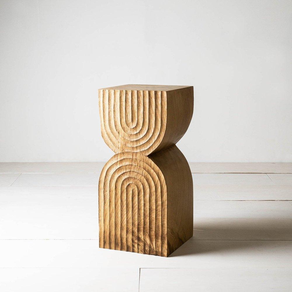 Aya Side Table by Mythology
Dimensions: D 24 x W 24 x H 52 cm
Materials: Reclaimed oak.

Featuring bold, architectural curves and intricate carved detailing, the Aya side table seamlessly blends functionality with artistry.
The piece is hand-carved