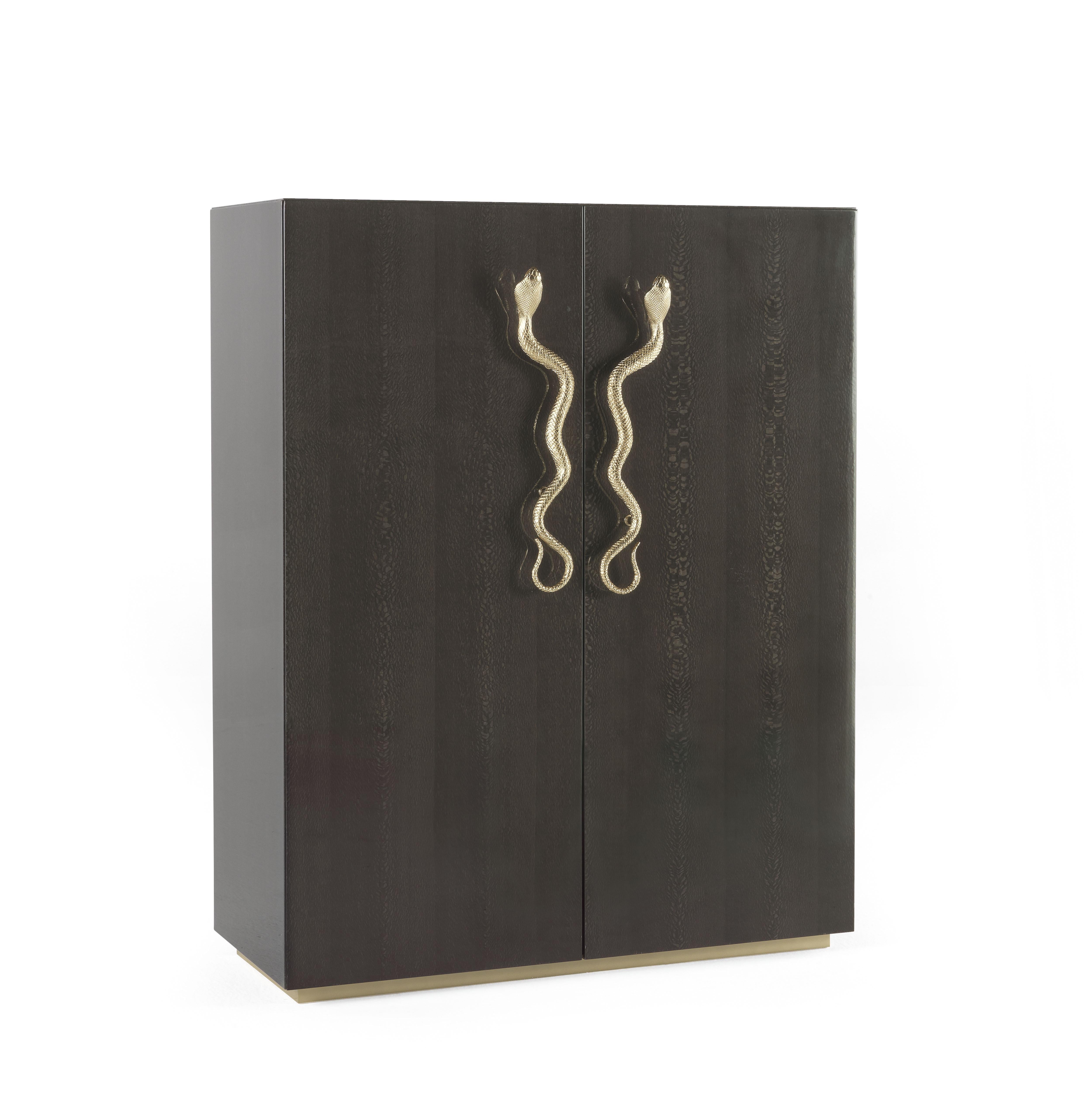 Azingo Bar cabinet with structure in multi-layer wood. Finishing in glossy carbalho grey color. Wooden base lacquered in gold finishing. Inside finishing in microfiber with smoked glass shelves and smoked mirrors. Snake “jewel handle” in cast brass