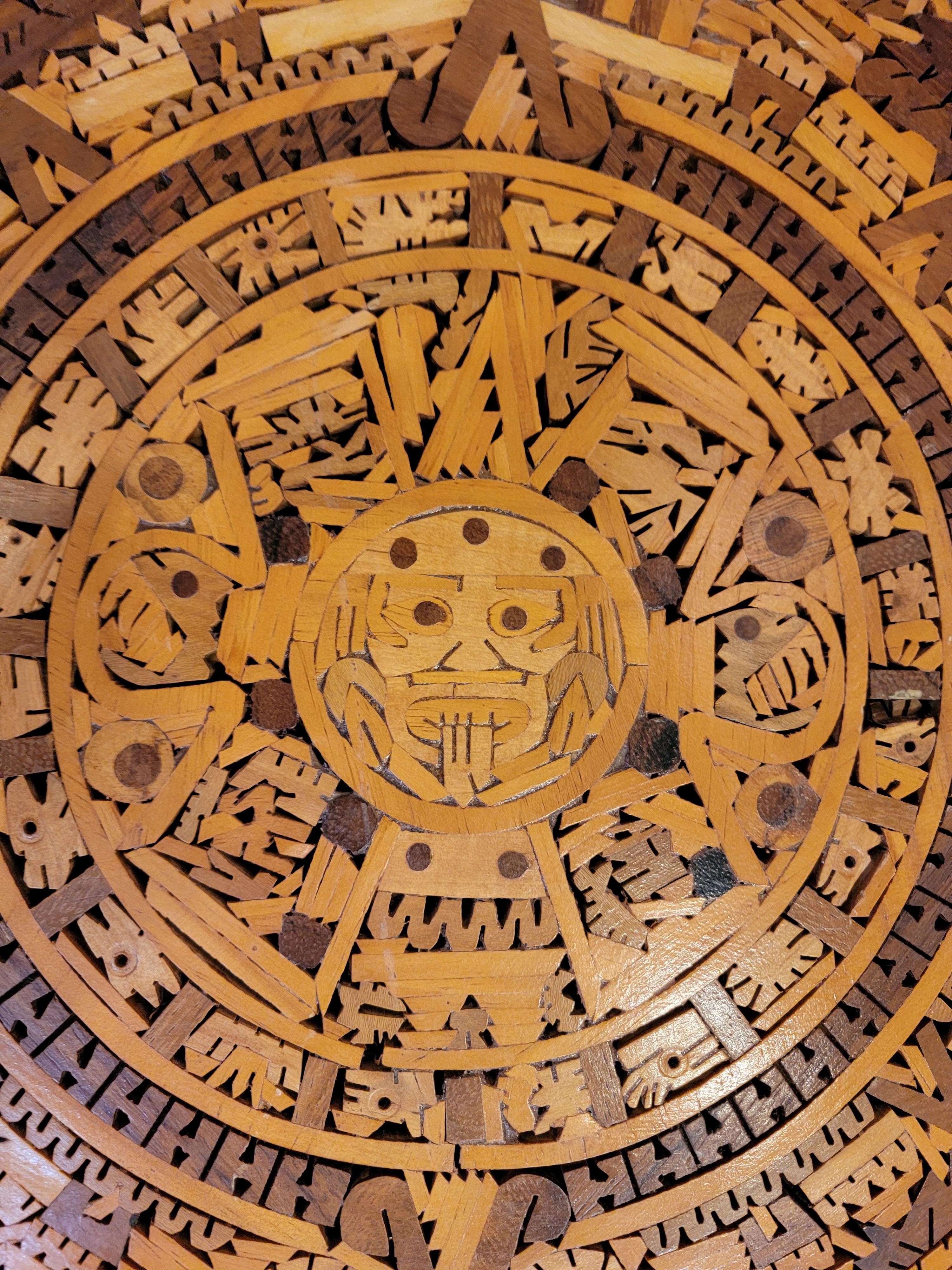 A hand crafted wood marquetry Aztec calendar. Made with multiple intricate pieces of exotic woods. Use as a wall hanging or decorative object.

18 inch diameter.
1.88 inches high.

Small chip of inlaid wood missing.