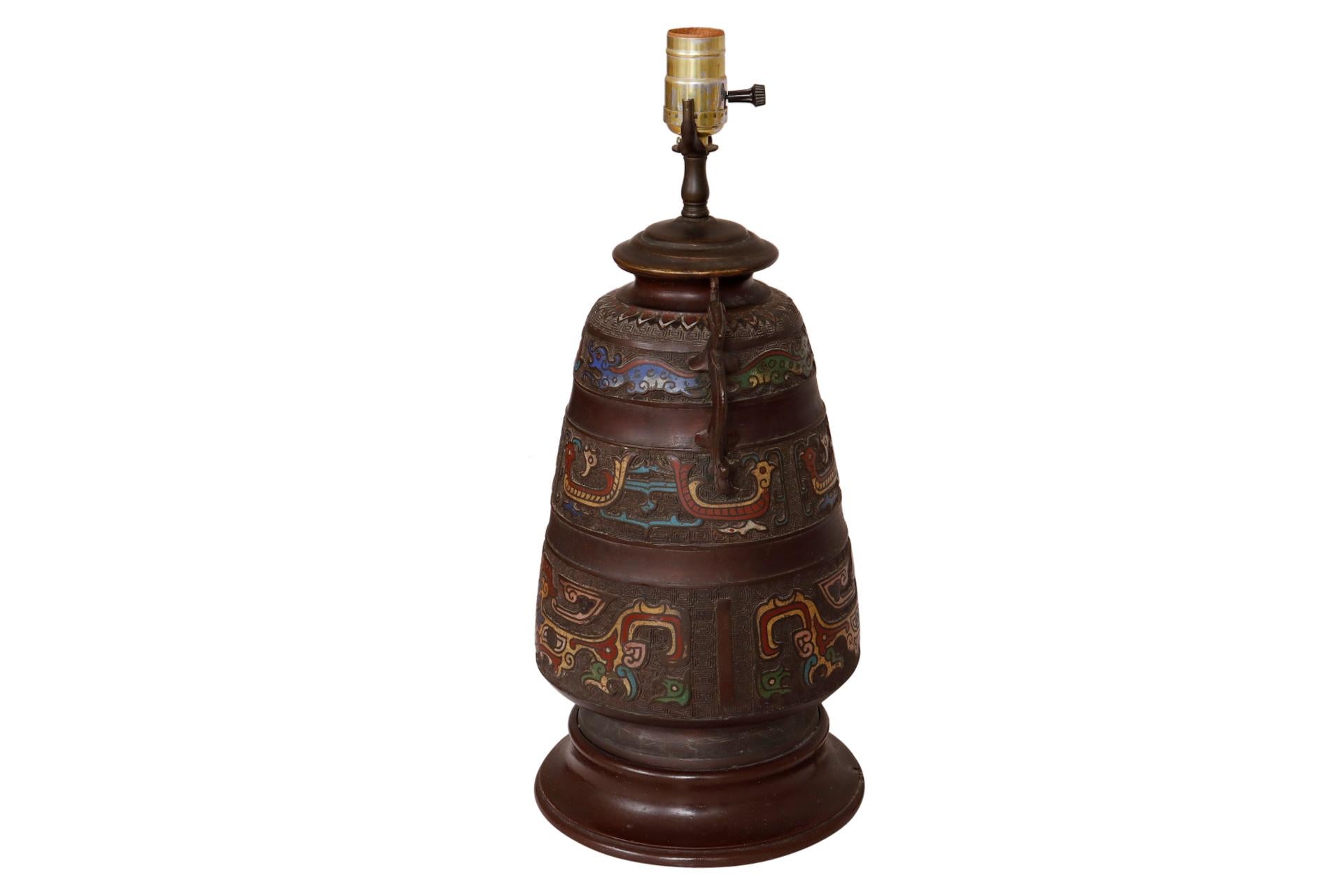 An Aztec inspired table lamp made of metal. Decorated throughout with finely cast pictorial animals in bold enamels in primary colors. Tapers upward with dragon like handles at the shoulder.
