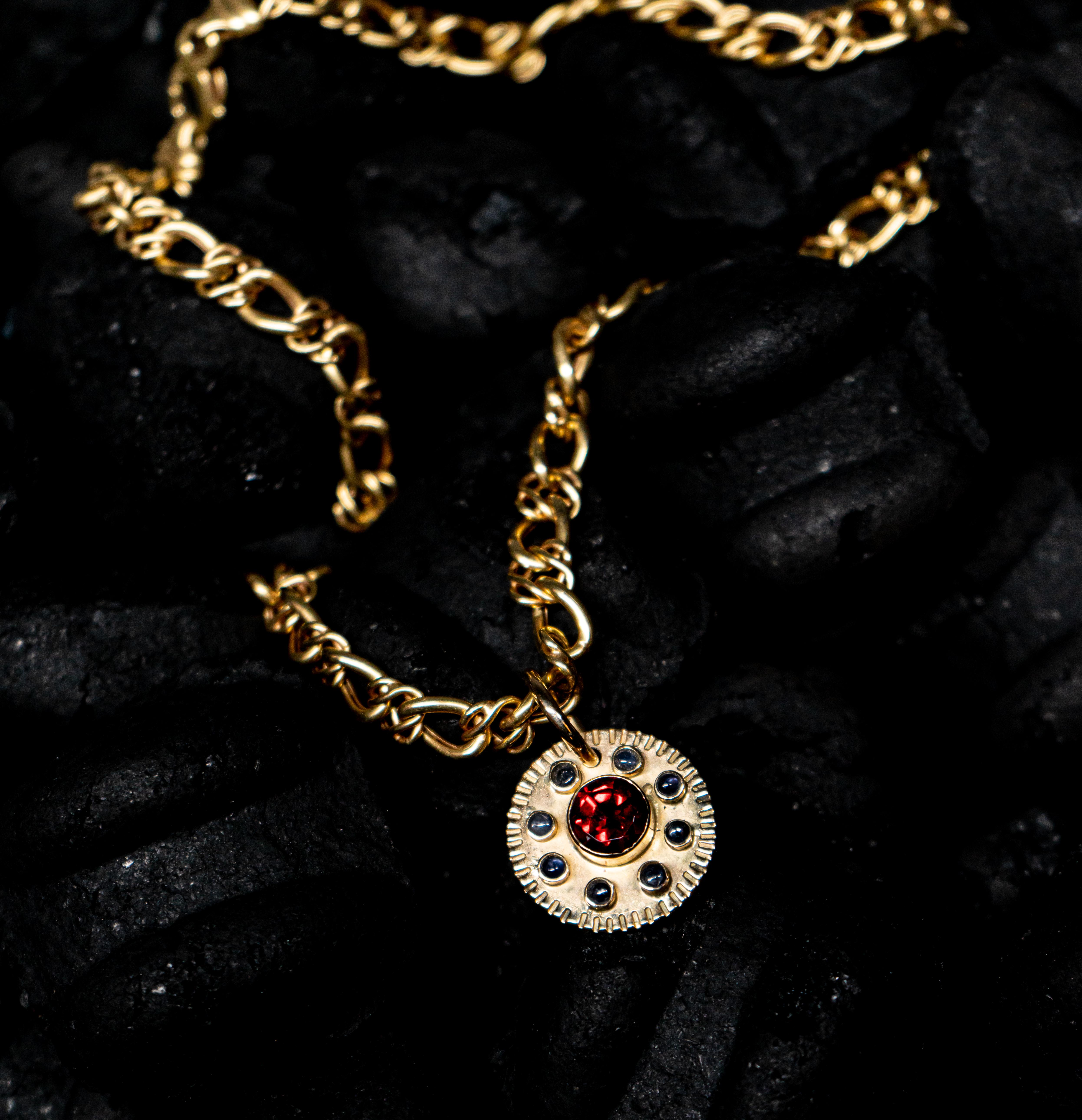 The aztec sun is highlighted pendant, with a weight of 10 grams of solid gold 18k, with a central granate of 0,30 carat and 8 sapphires that surround the central stone is a artesian design inspired by aztec culture of mexico.
