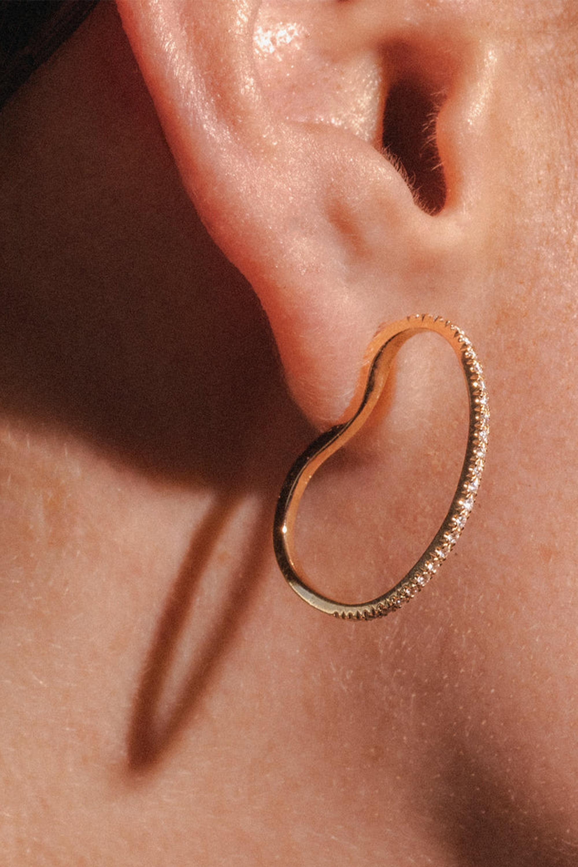 These mesmerizing Azura earrings offer a fresh take on the classic hoop, crafted in 18k rose gold and adorned with 0.5ct of dazzling diamonds. At first glance, they appear as graceful loops, but as you shift perspectives, their organic, floating
