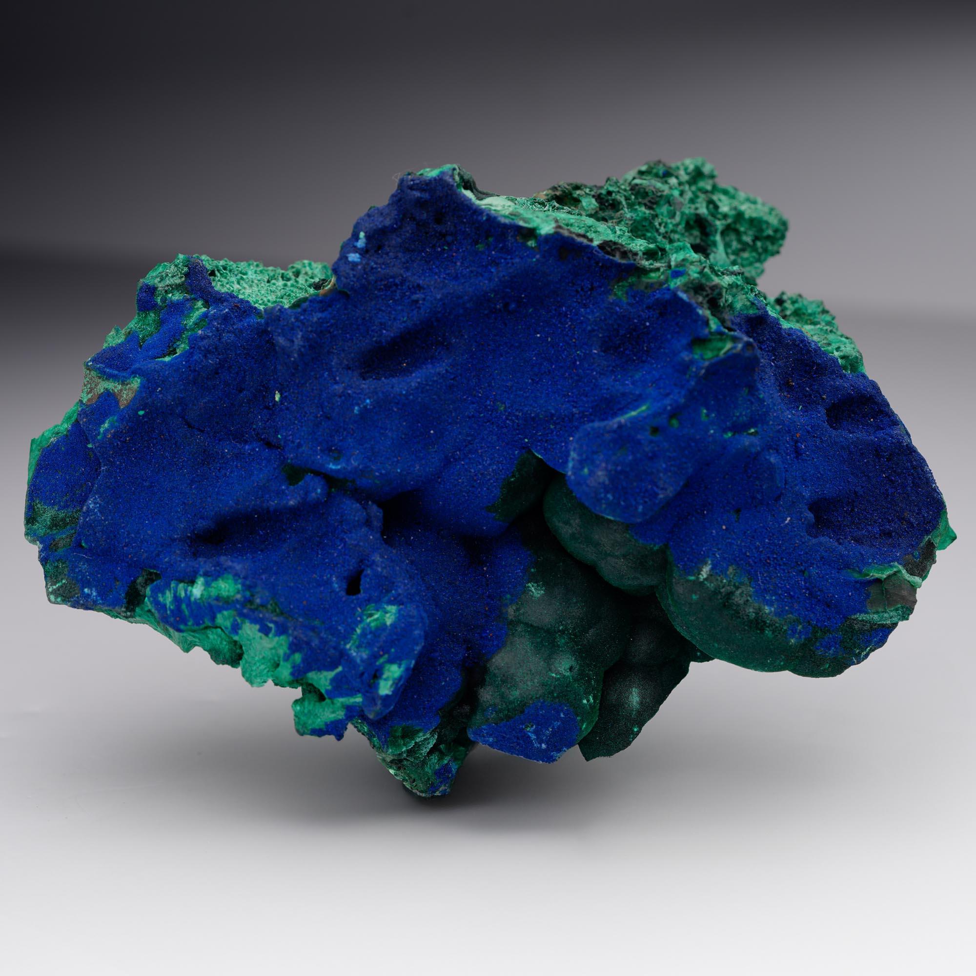 Questo esemplare di azurite su malachite proveniente dalla Cina pesa 1,46 libbre e presenta un drammatico gioco di tonalità di blu reale intenso e verde vibrante. L'Azurite, riccamente drusa, ricopre gran parte della superficie con un'intensità
