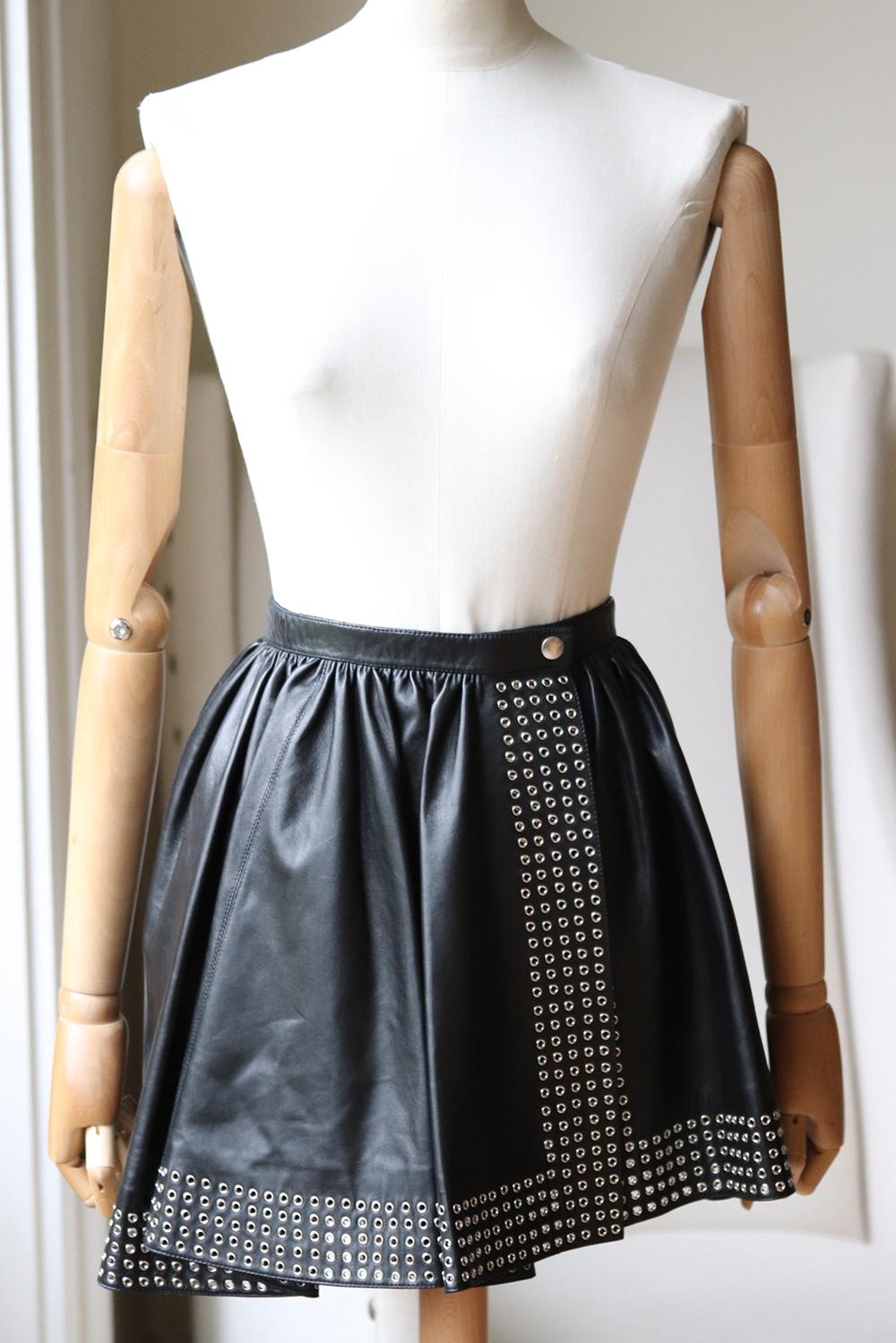 This beautiful Alaïa skirt has been engineered for the perfect fit, it is made from structured leather and traced with silver eyelets along the hem. 
Black leather.
Snap fastening at front.
100% Leather (Lamb); lining: 100% nylon.
Comes with