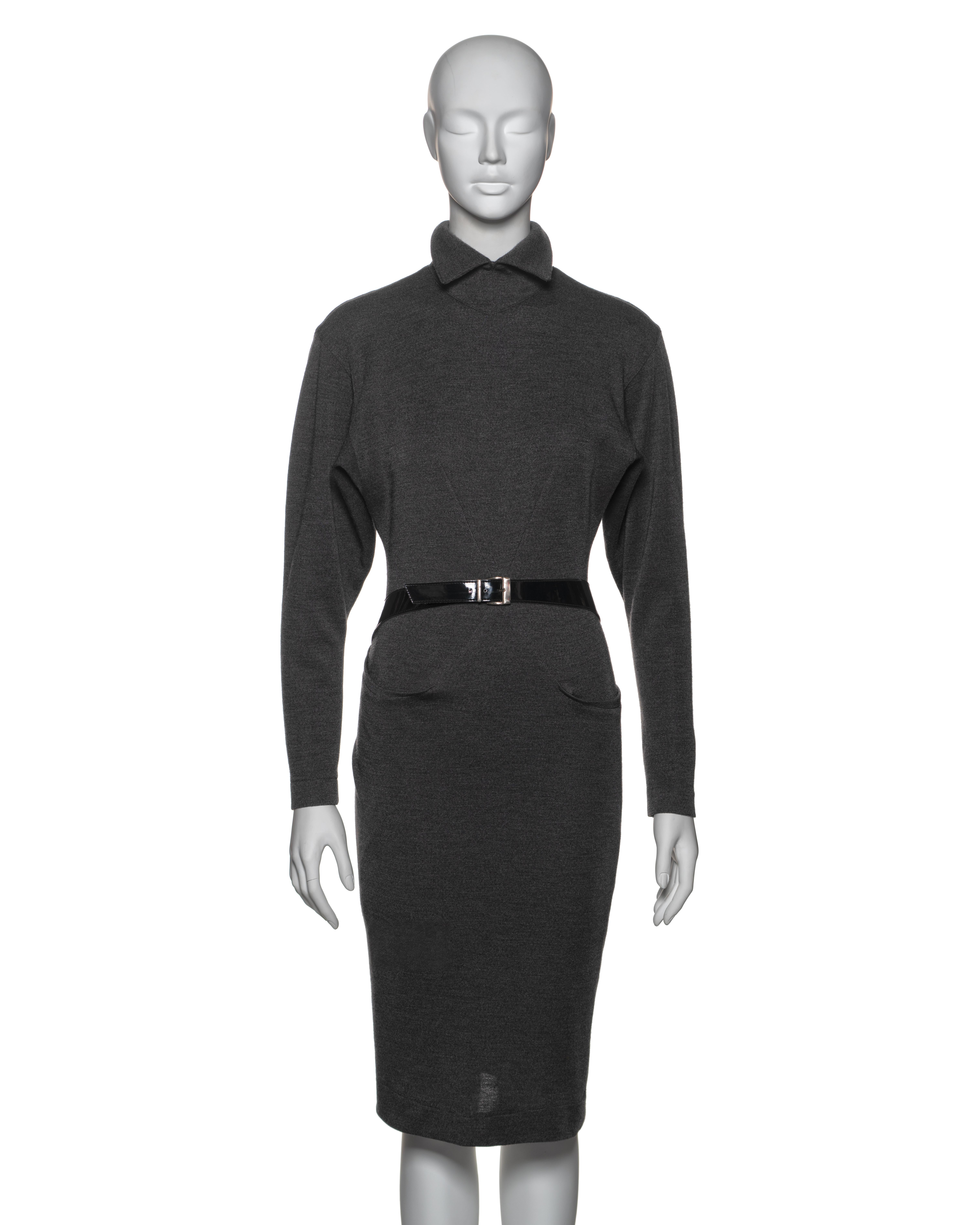 This early Azzedine Alaïa design is crafted from charcoal grey wool, showcasing the designer's signature fitted silhouette. It features a high neckline with a folded collar and long sleeves. The lower part of the dress is designed as a wrap skirt,