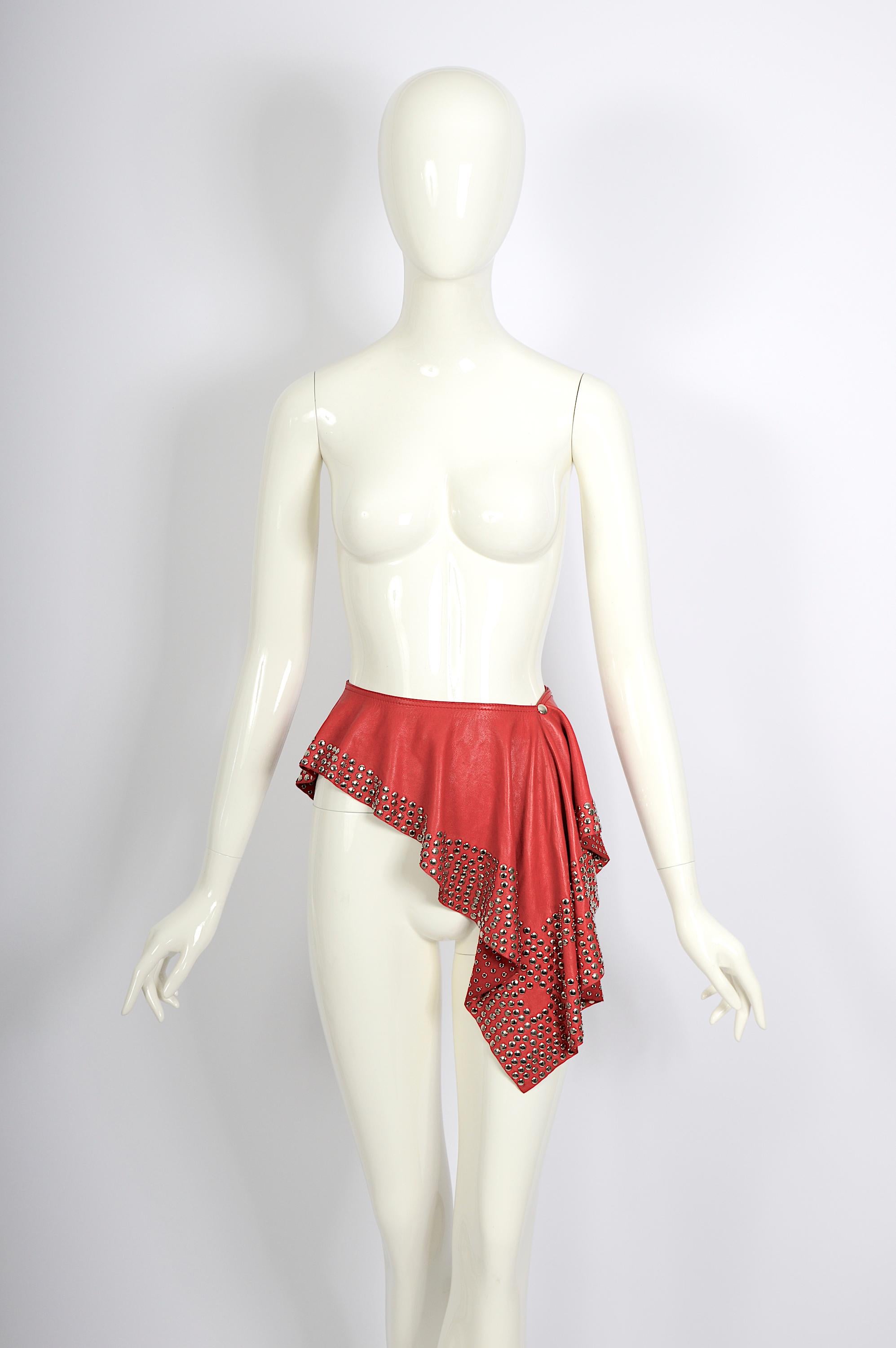 Upgrade your Azzedine Alaïa collection archive with this important, exceptional, unique vintage Alaïa red leather belt skirt from circa 1981.
Made from lambskin leather, it features a chic waist drape embellished with metallic studs. 
The skirt has