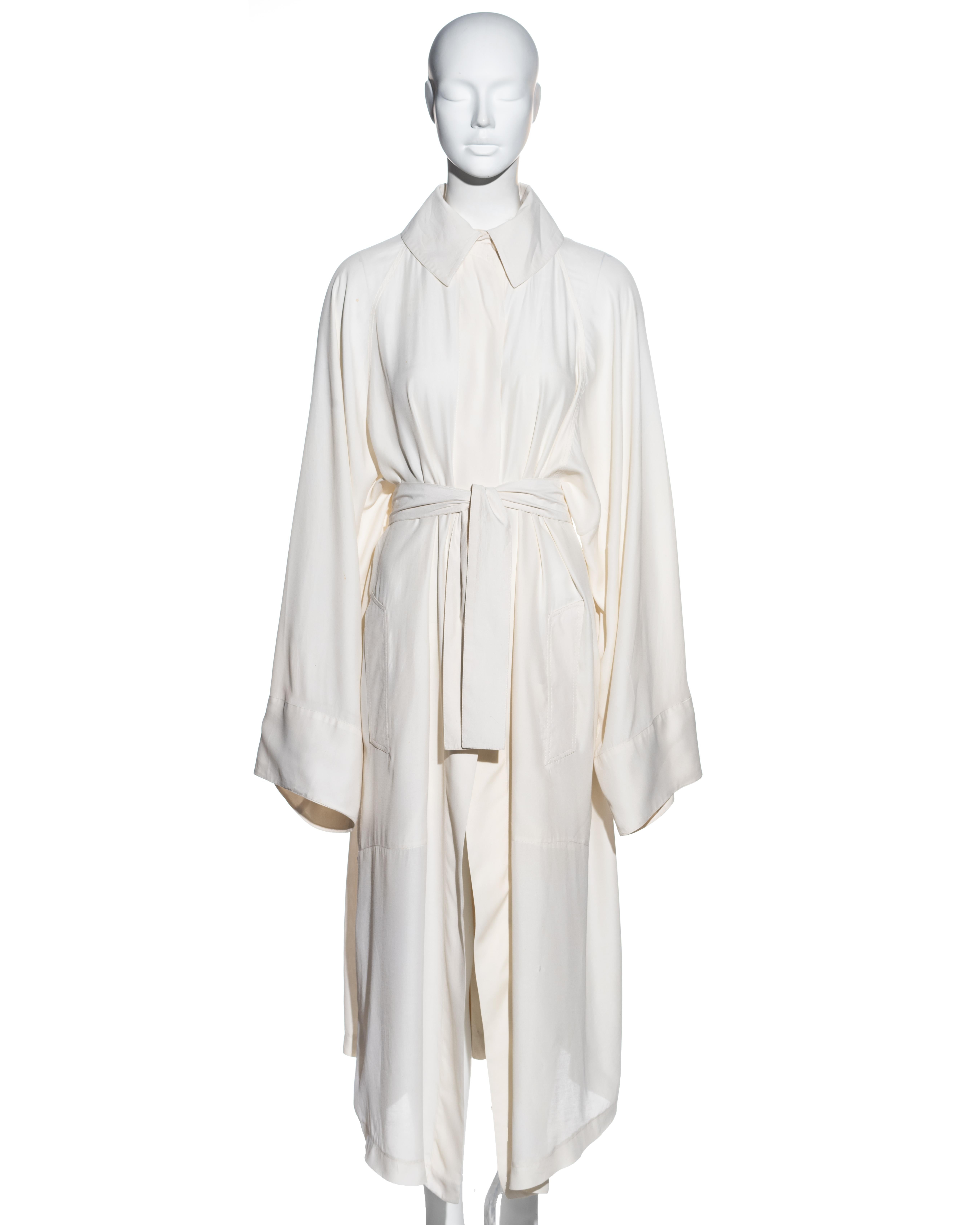 ▪ Azzedine Alaia cream cotton coat dress
▪ 2 button fastenings at collar 
▪ Wide cut sleeves 
▪ Voluminous shape 
▪ Pleated wrap skirt attached to back panel fastening with two long bands at the waist 
▪ Button fastenings on skirt 
▪ Vertical slit