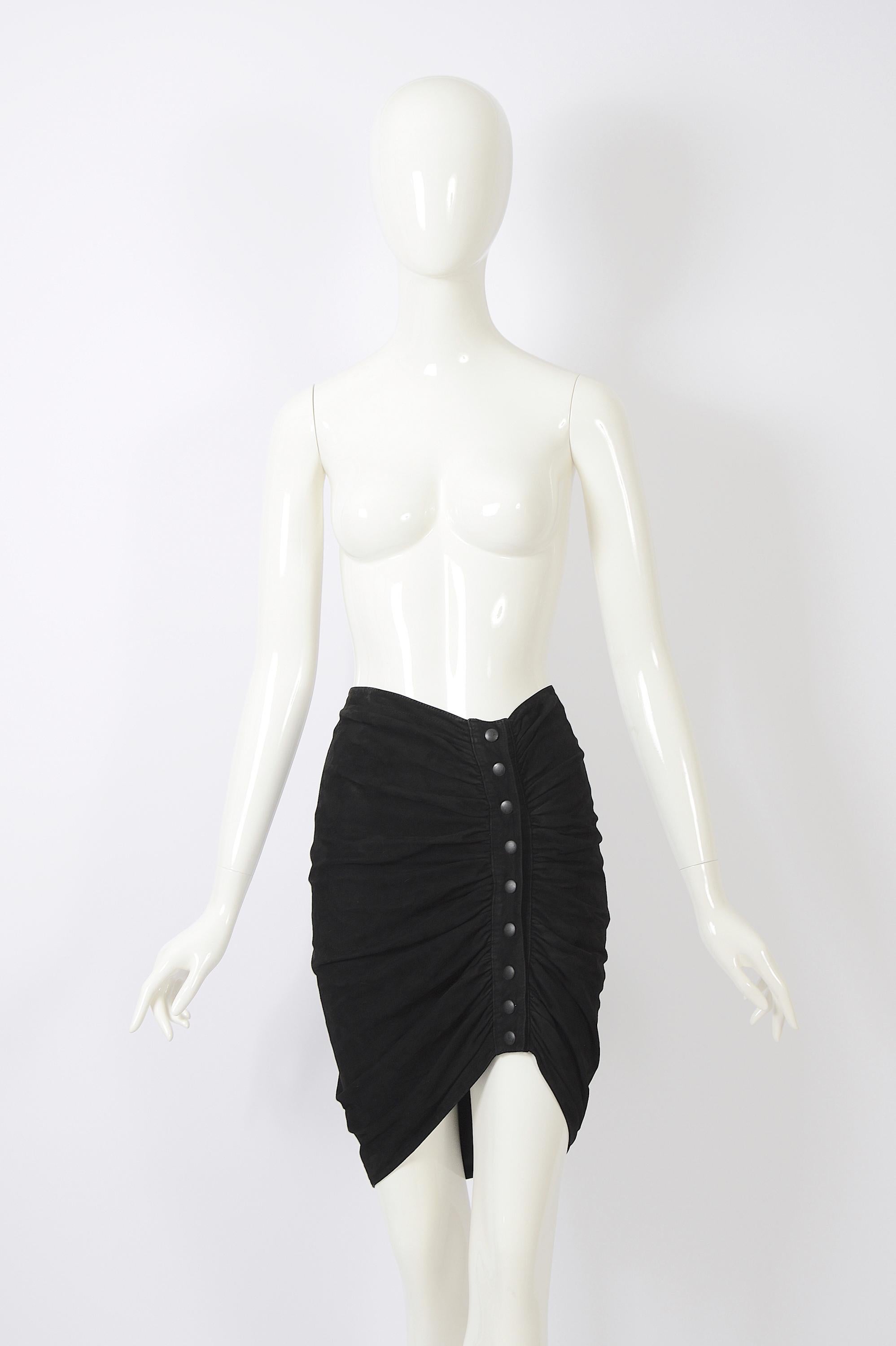 This skirt is a rare piece from Azzedine Alaia's vintage Fall/Winter 1983 collection, showcasing the early years of his incredible career. Crafted from black suede, it features a fitted silhouette and an asymmetric hemline. The draped front opening